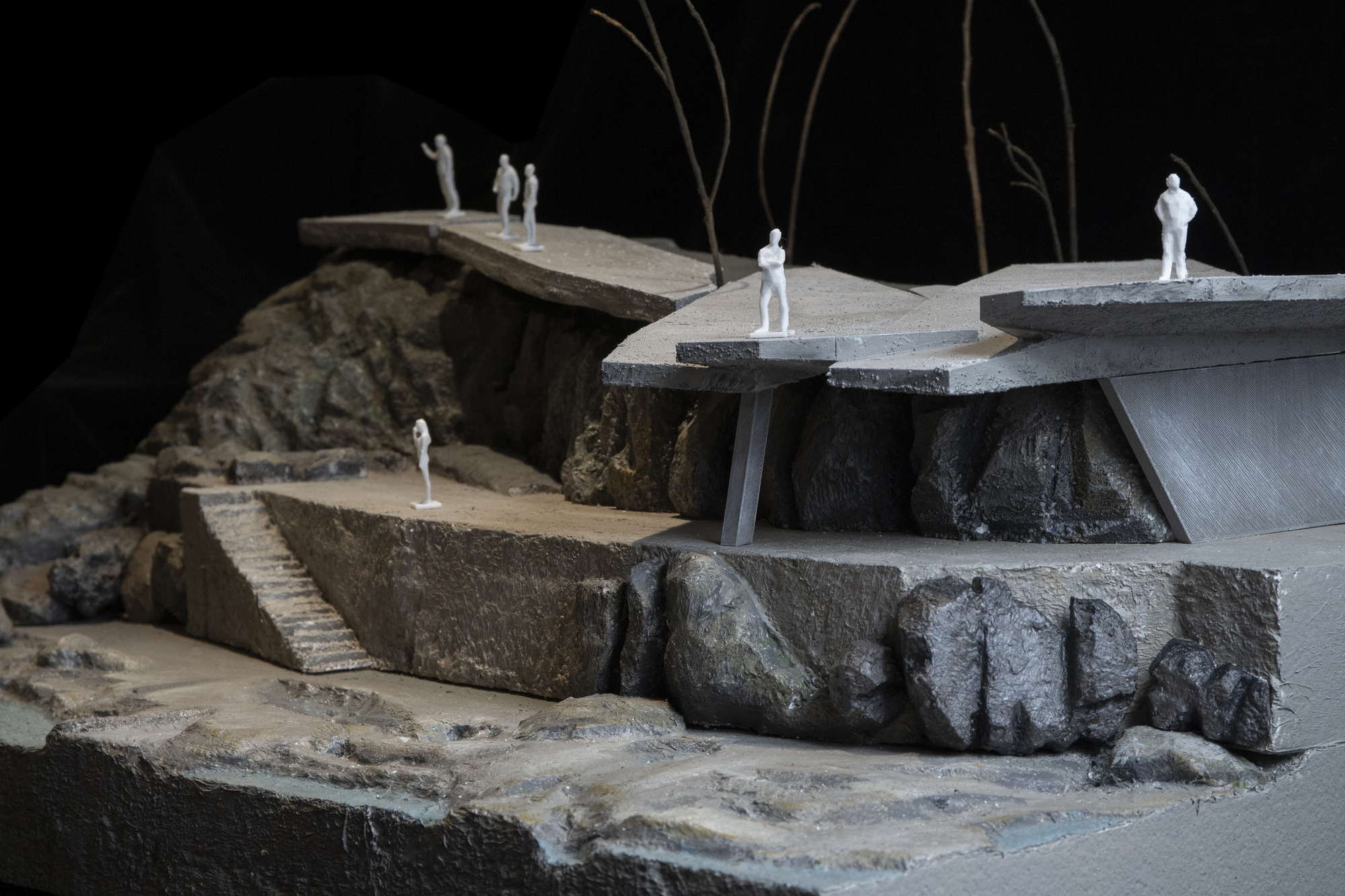 Side view of the model revealing multiple cantilevered levels with figures standing on terraced platforms