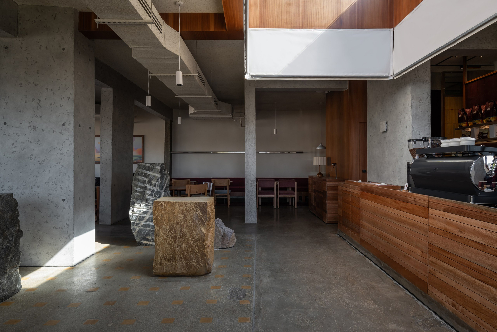 Interior space with a central skylight, concrete columns, timber millwork counter, and large boulder fragments scattered across the floor