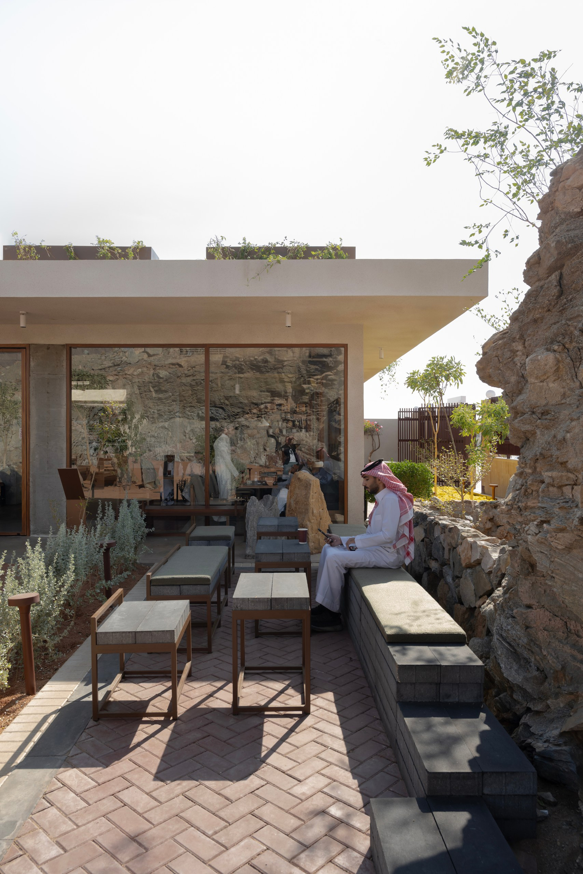 Outdoor terrace with herringbone brick paving and glazed doors opening to an interior with figures seated inside