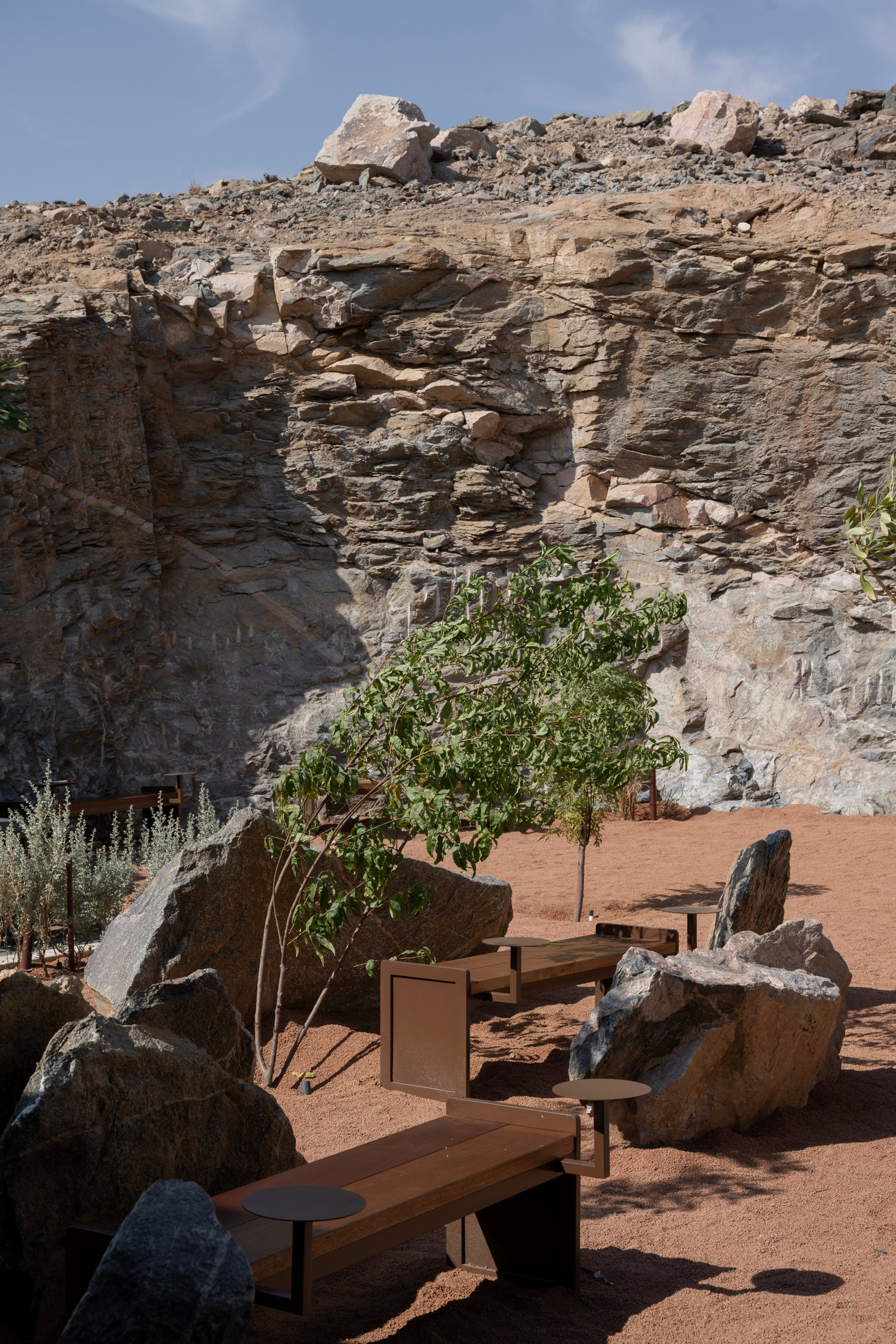 Reddish sand terrace with timber benches and planters nestled against weathered rock formations