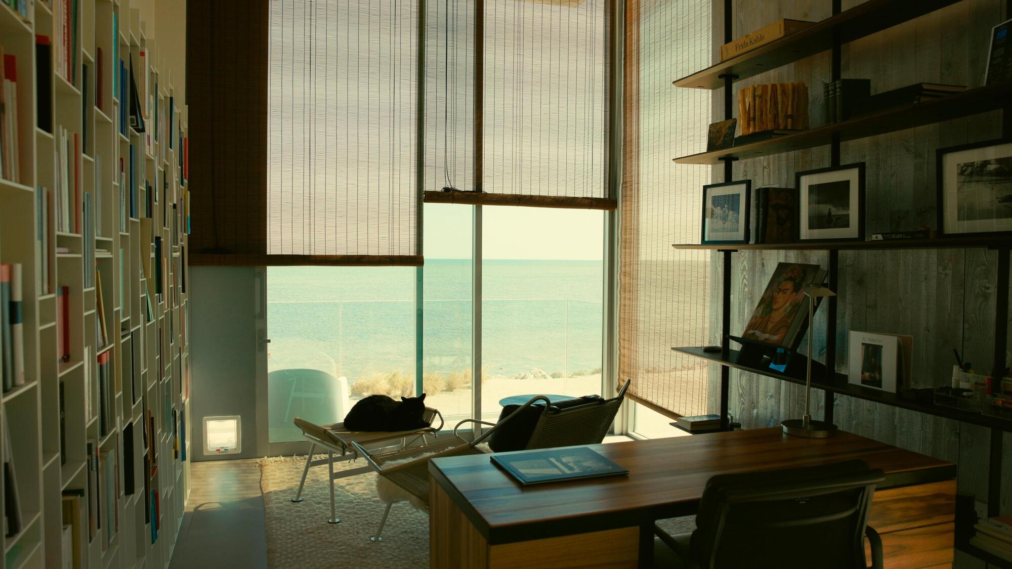 Interior workspace with timber desk and floor-to-ceiling window overlooking the ocean through translucent shades