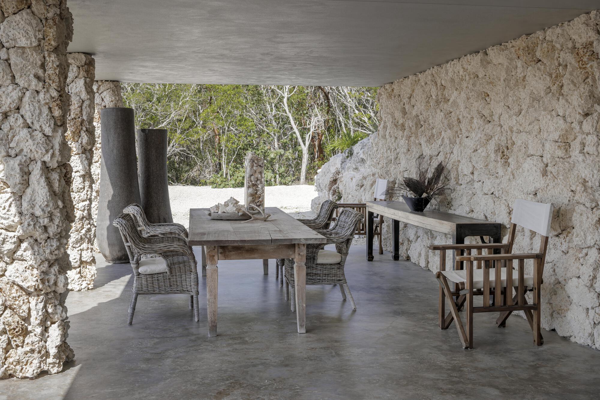 Covered terrace with textured coral stone walls, polished concrete floor, and dining furniture beneath a smooth ceiling