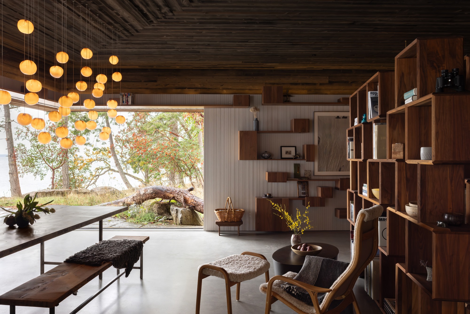 Living area with clustered sphere pendants and timber shelving looking out to lakeside clearing in autumn