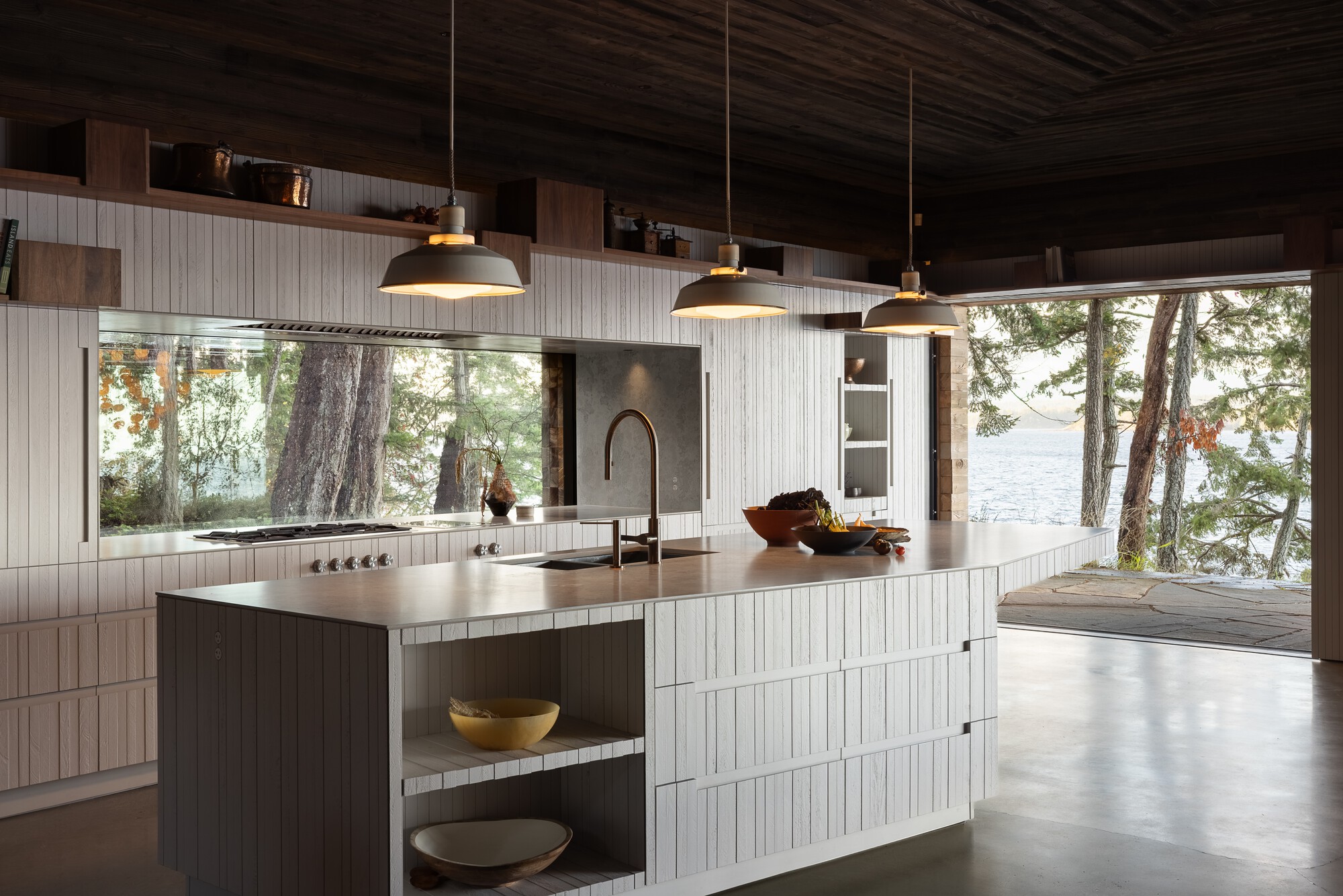 Kitchen island with pale vertical-board cabinetry and wide window overlooking lakeside trees