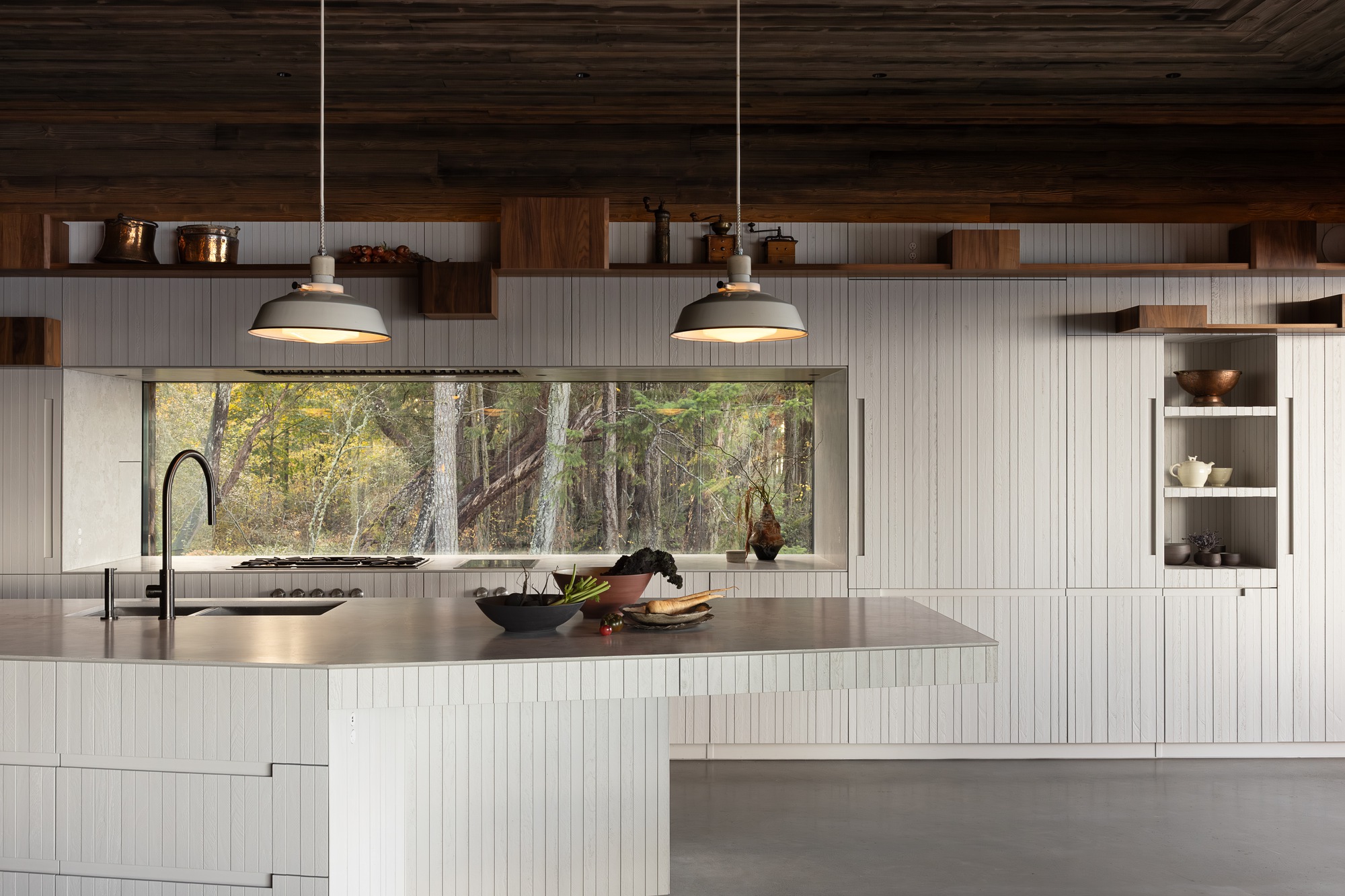 Kitchen counter with stainless steel top and horizontal window view into wooded landscape