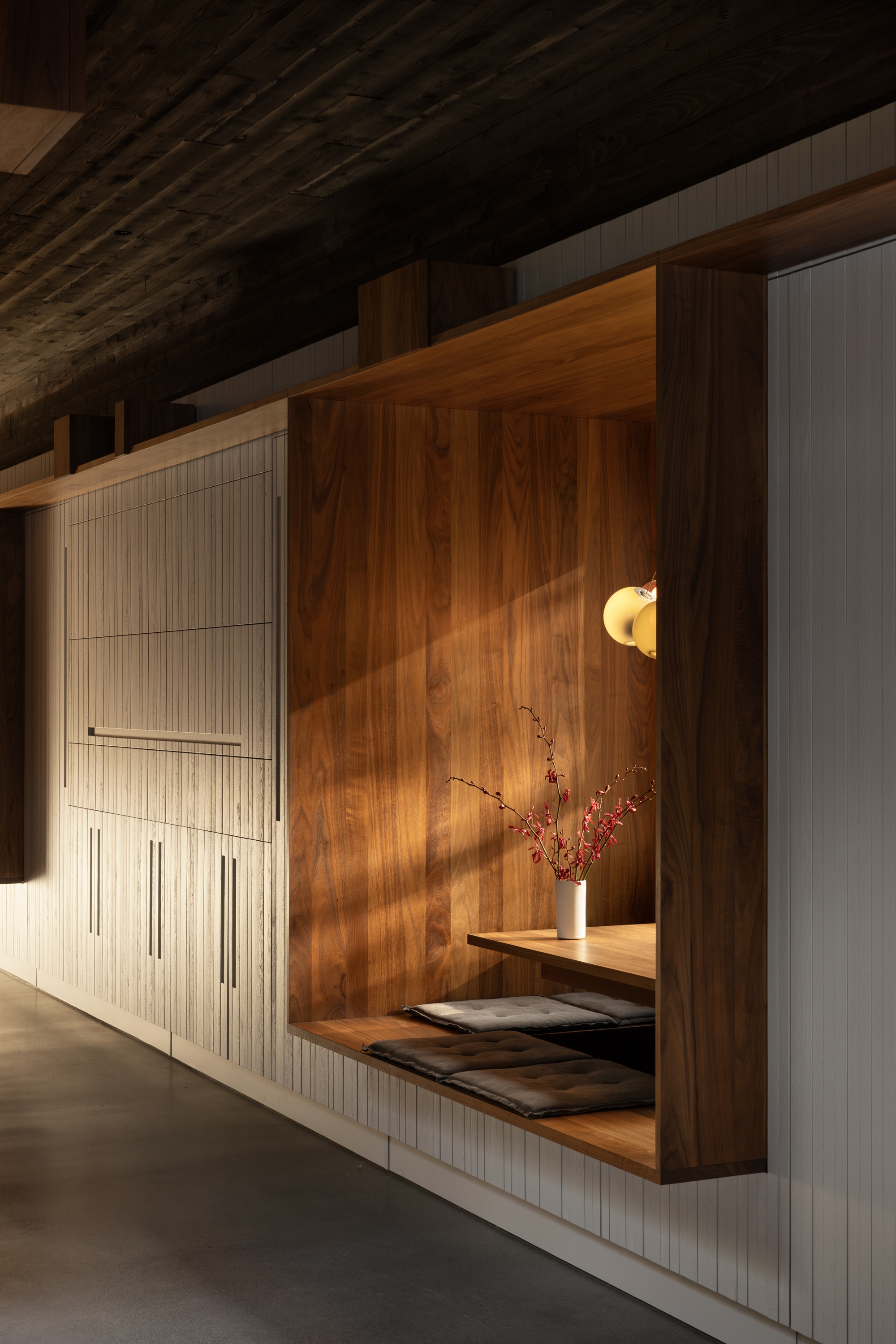Built-in walnut storage wall with recessed display niche and wall sconce under exposed timber roof beams