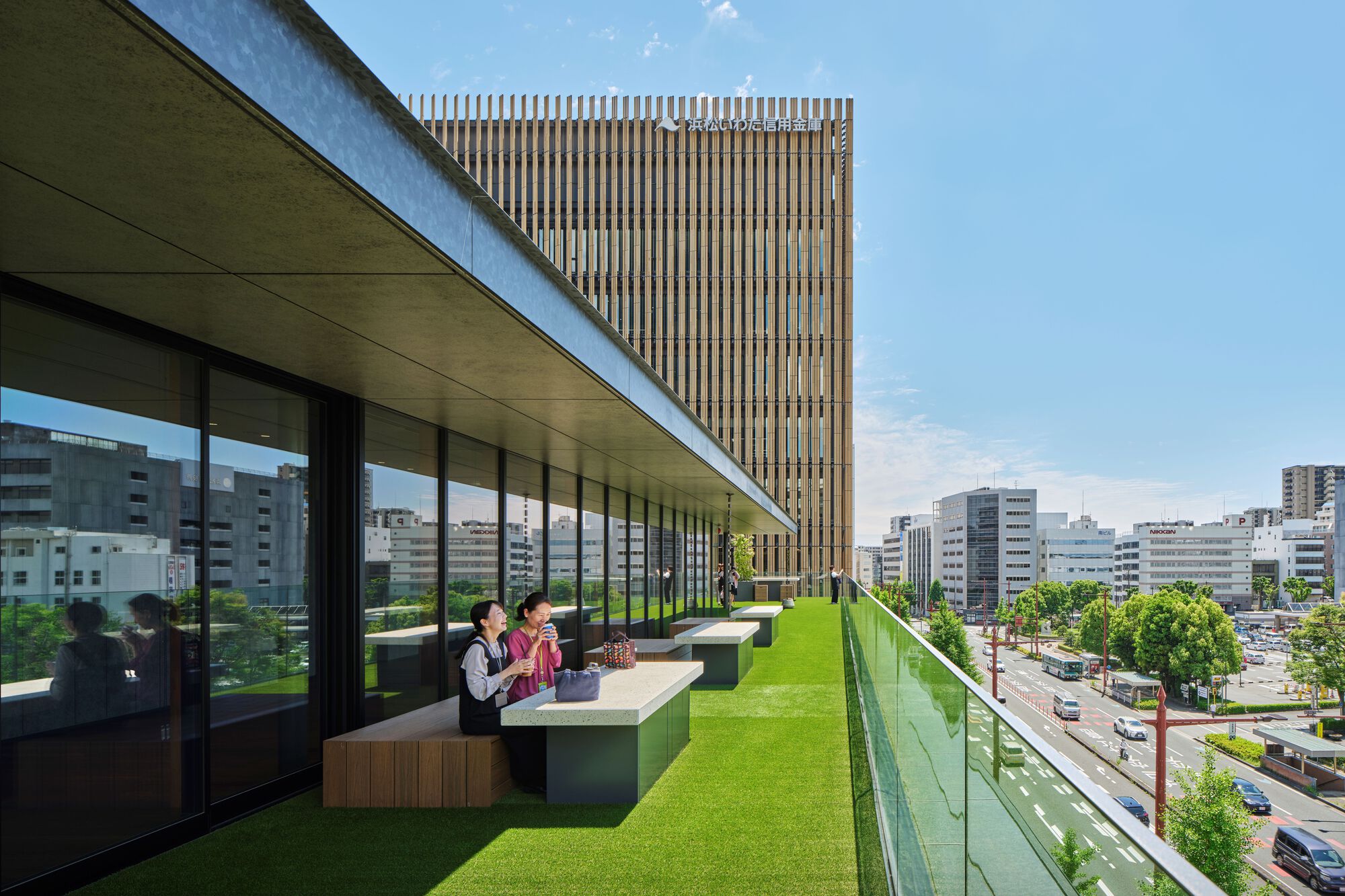 Rooftop terrace with artificial grass, bench seating, and glass balustrade overlooking the surrounding cityscape