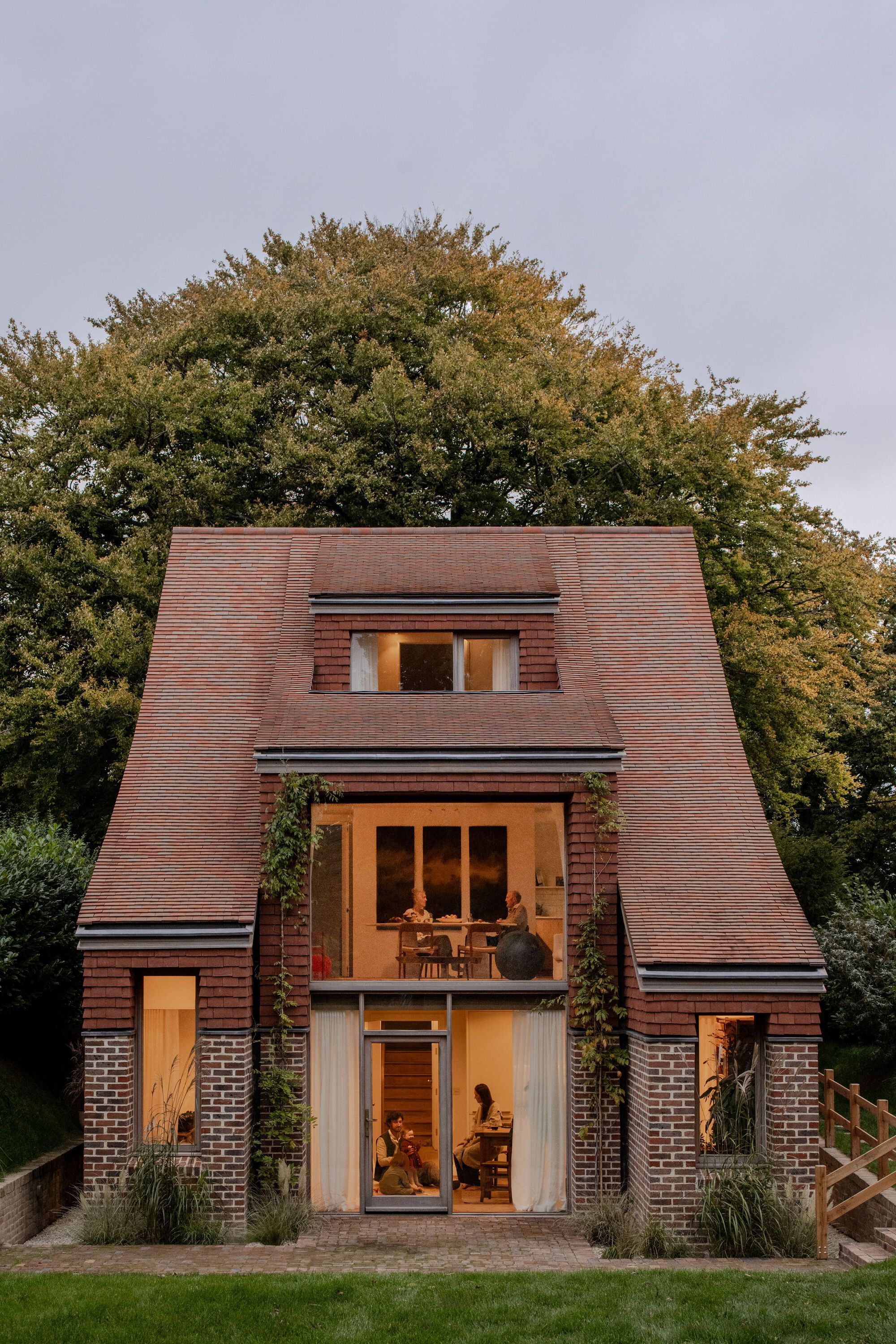 Front elevation showing stacked glazed openings and inhabitants visible inside at twilight