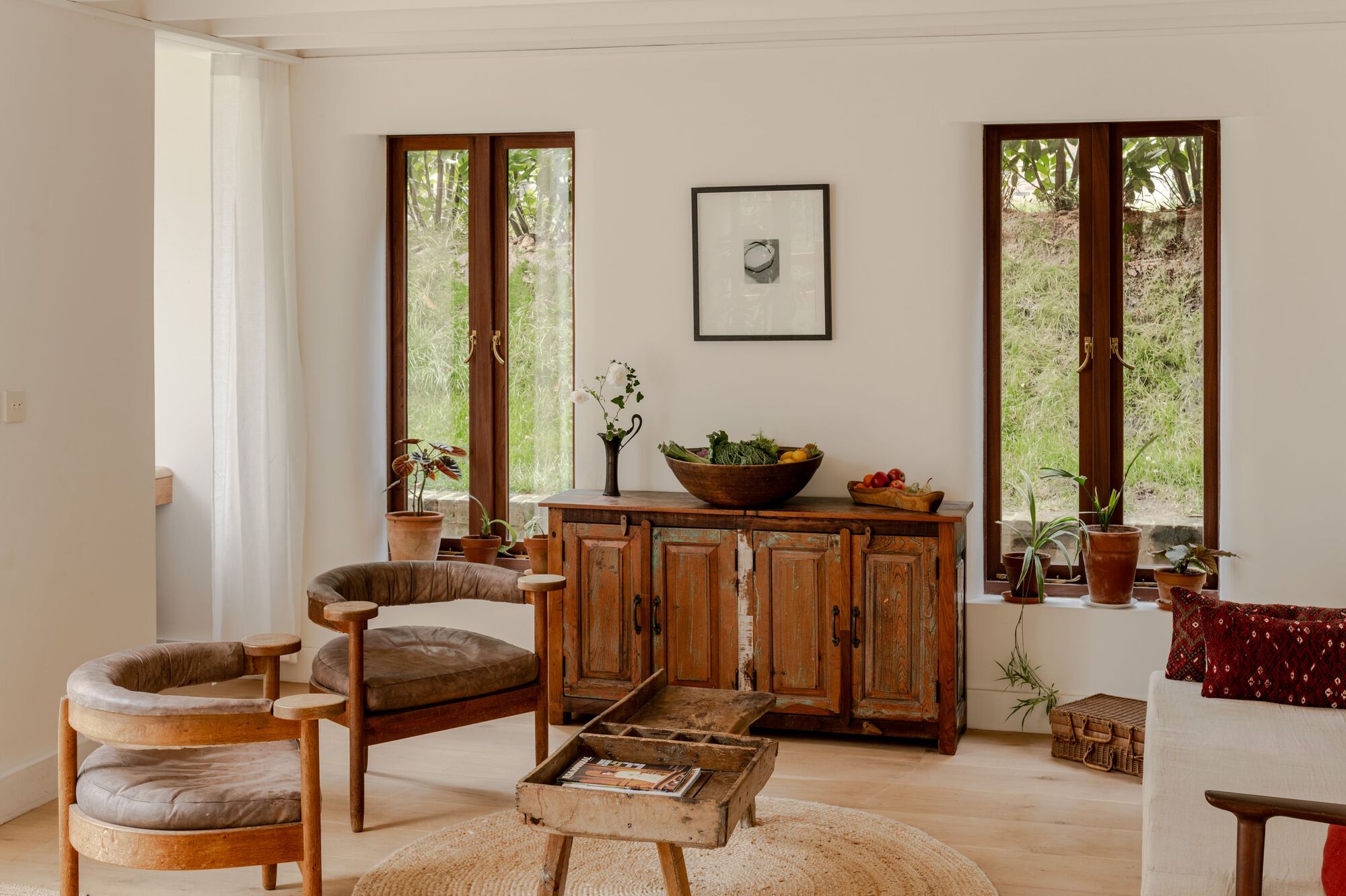 Sitting area with antique cabinet and paired timber casement doors framing views of native grasses outside