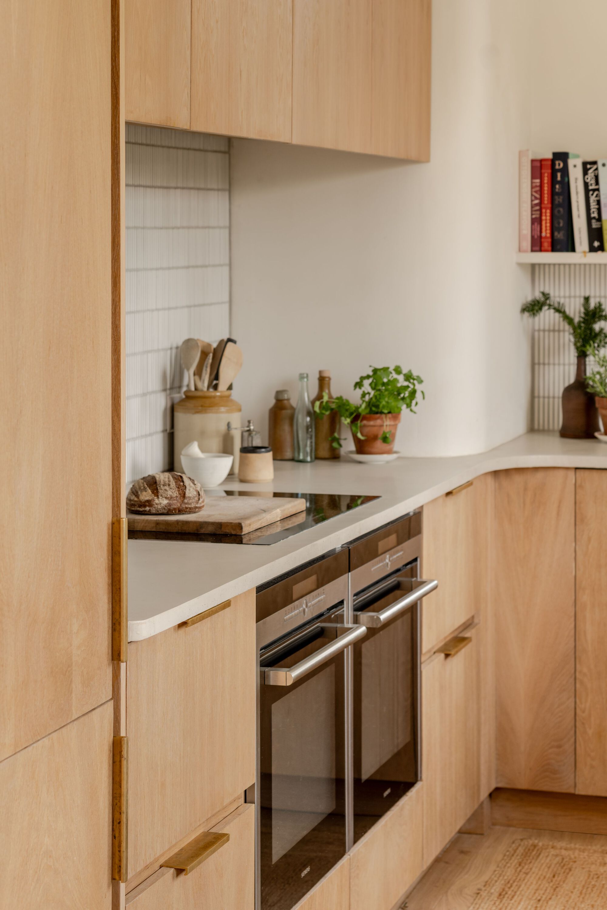 Kitchen corner with light wood cabinetry, white tile backsplash and potted herb on the countertop