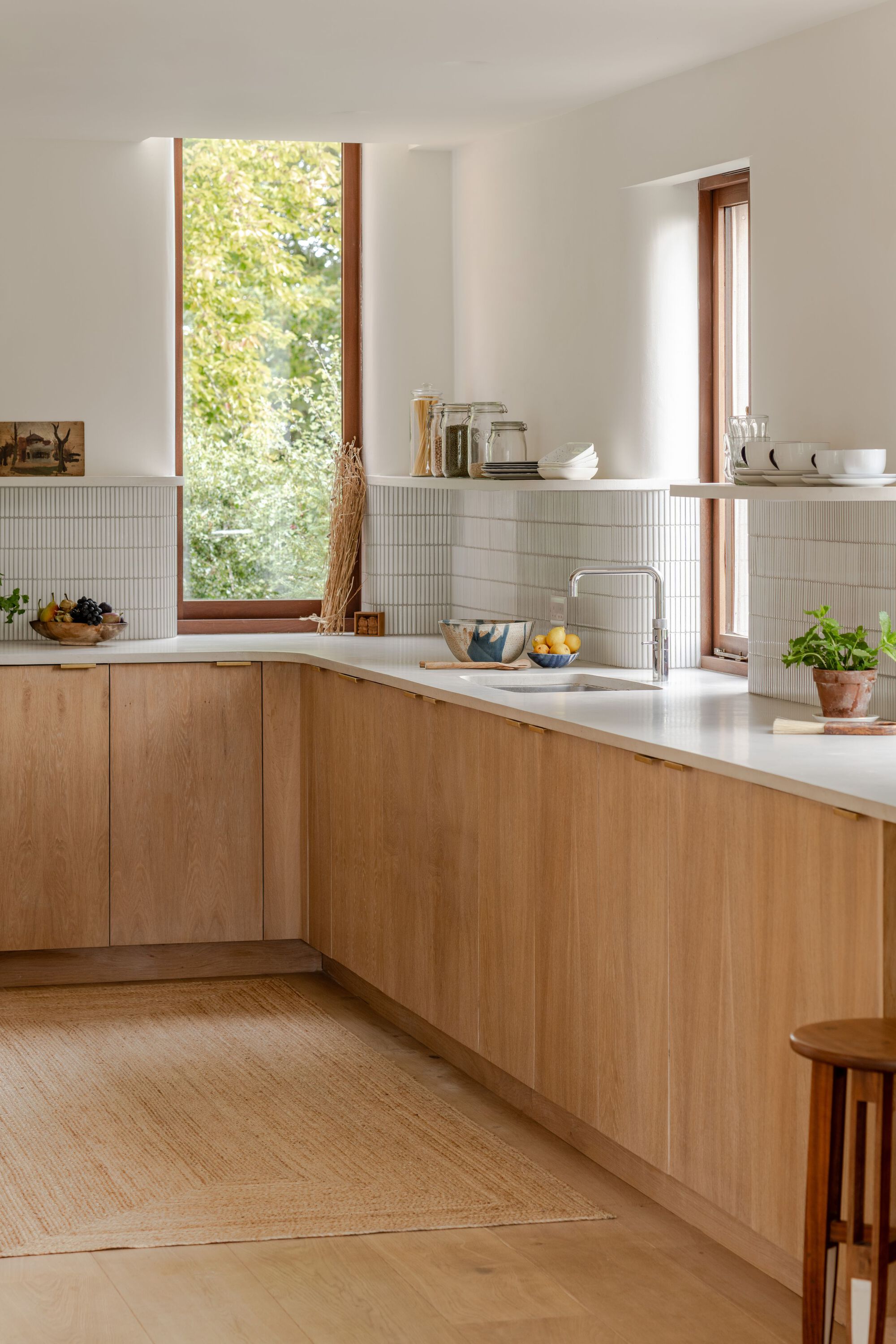 Kitchen with oak cabinetry and white tile backsplash framing a tall window looking onto green foliage