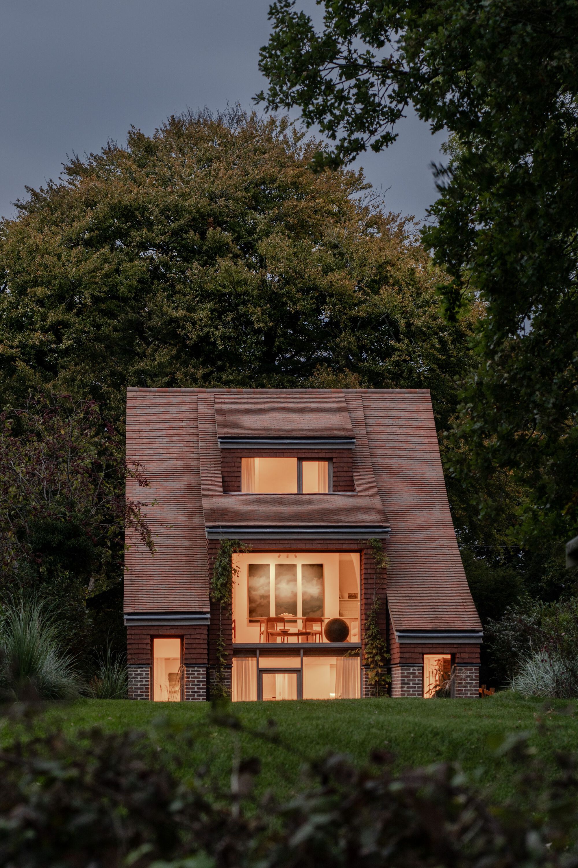 Garden facade with lit interior spaces visible through triple-height glazing at evening