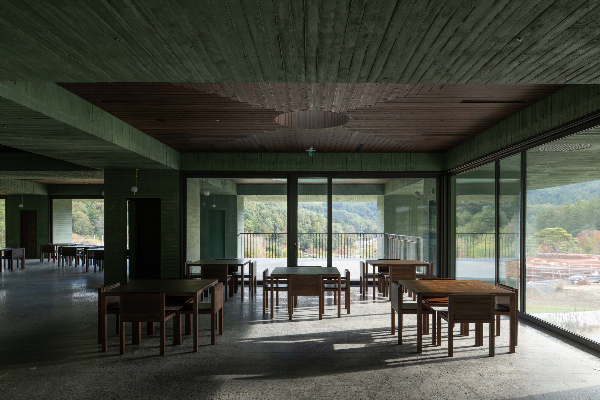 Interior dining space with timber tables and chairs beneath a green wood-paneled ceiling with circular aperture