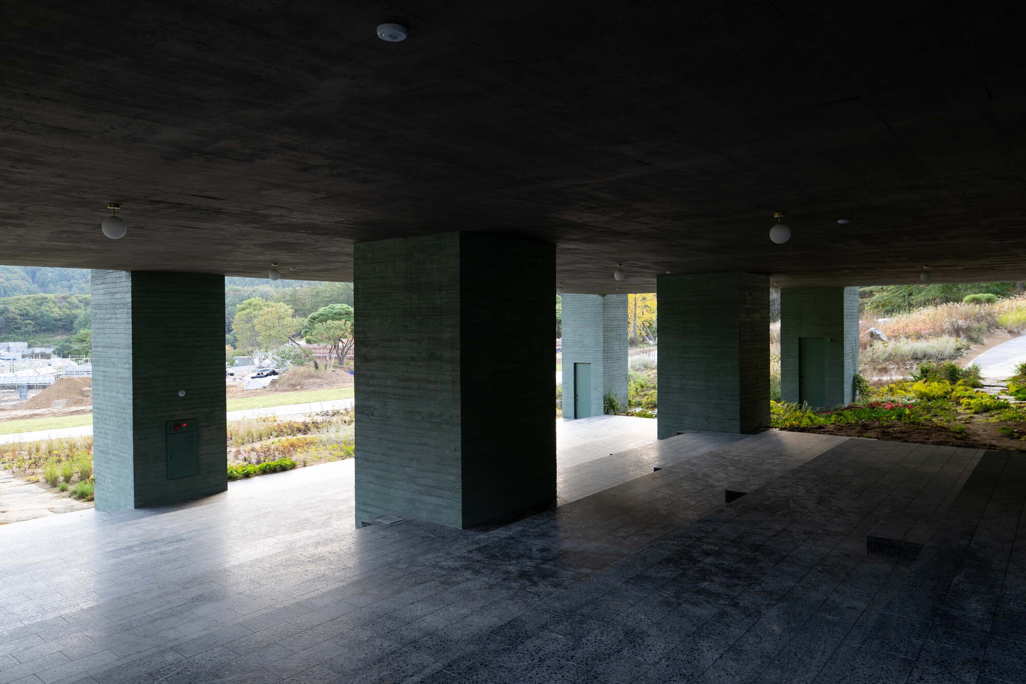 Covered ground level terrace with board-formed concrete columns framing views to landscaped beds beyond