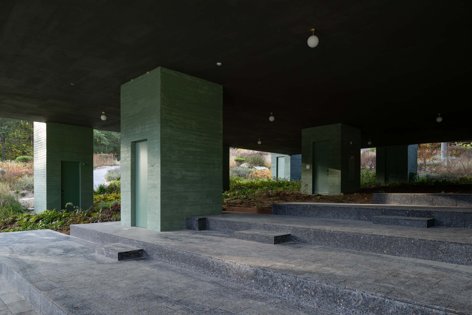 Stepped terrazzo platforms with green concrete service towers beneath the elevated building volume