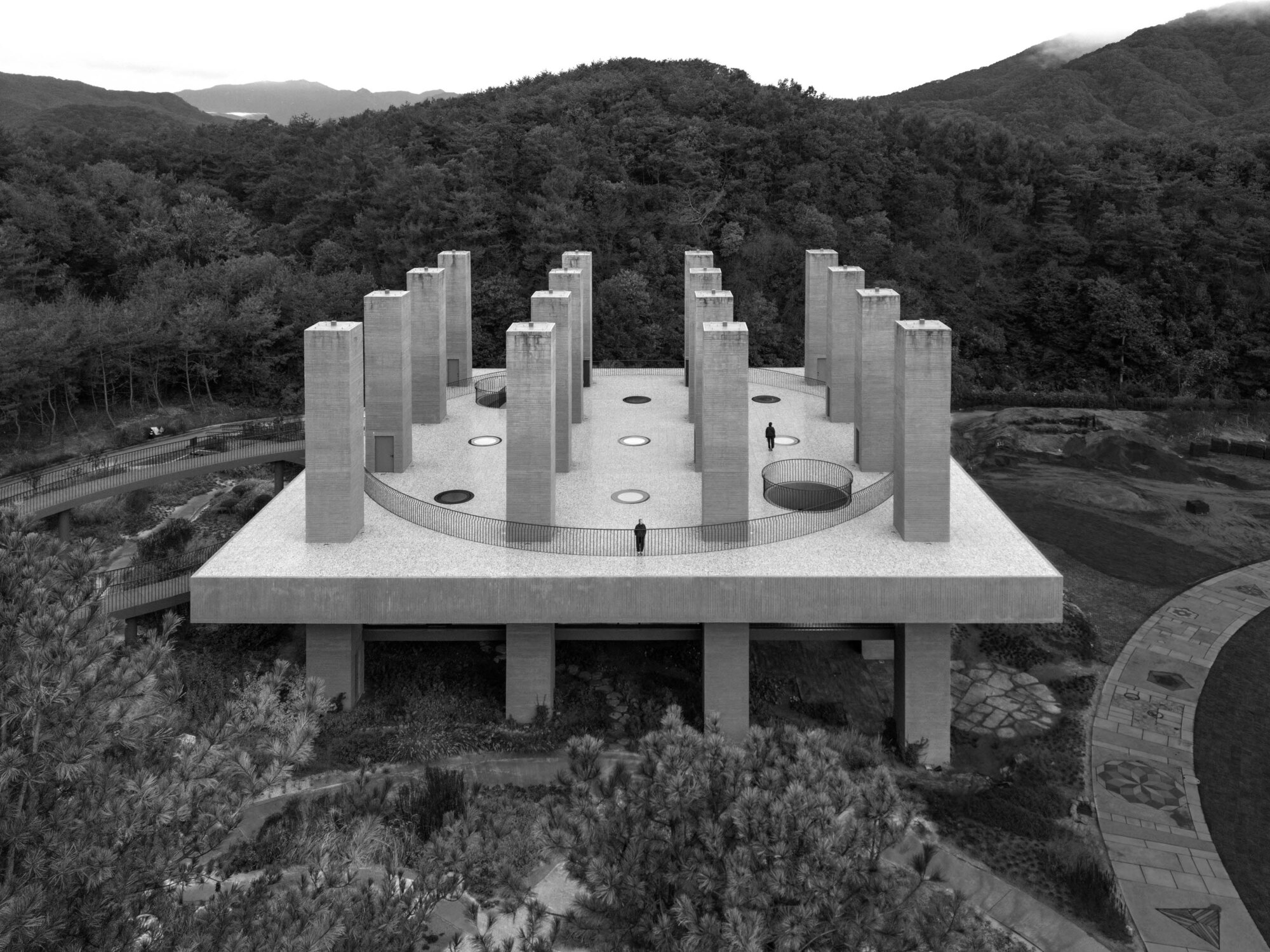 Aerial view of concrete roof with circular openings and tower groupings against forested mountains