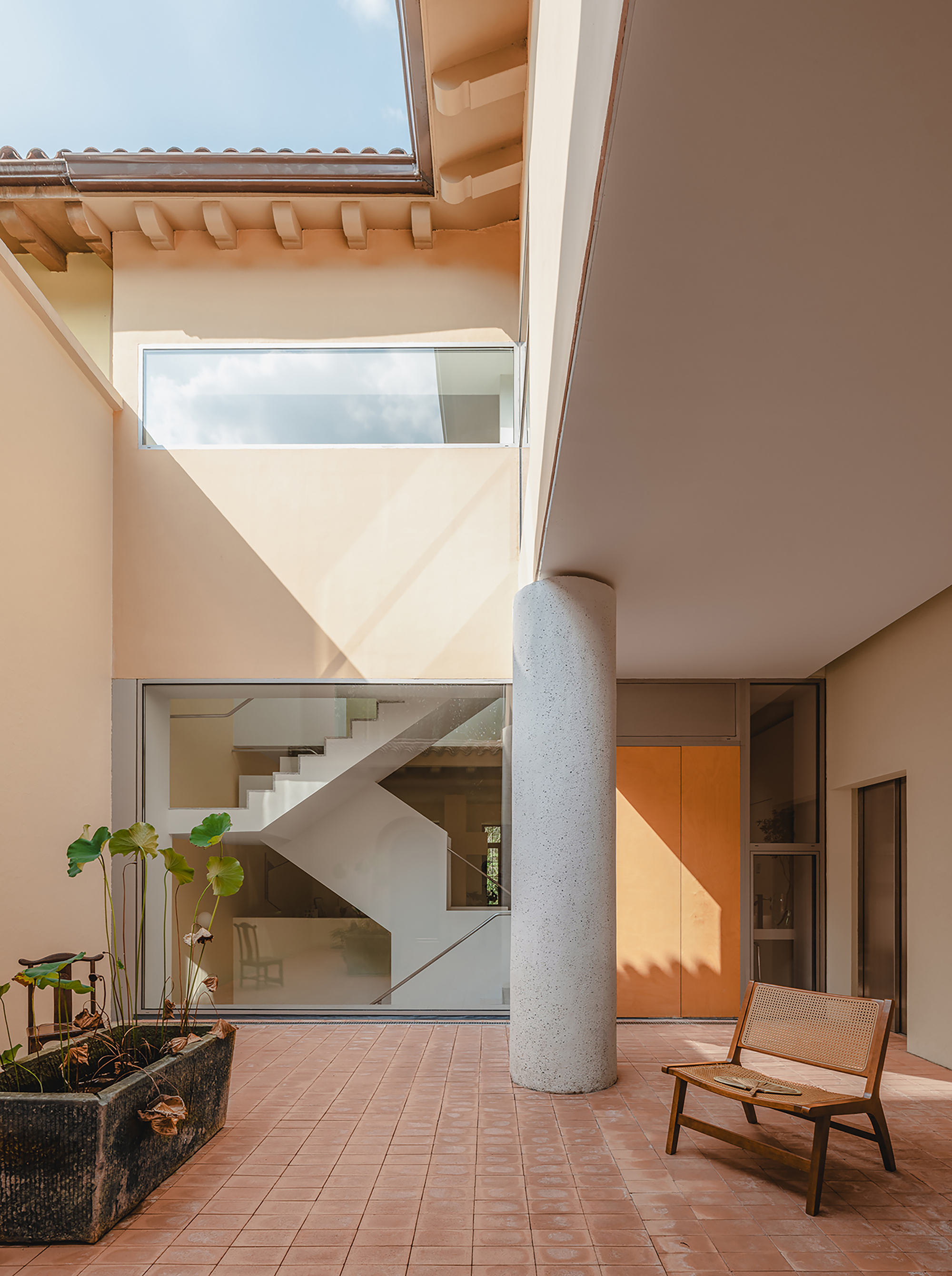 Terracotta tile courtyard with cylindrical concrete column and view to interior staircase above