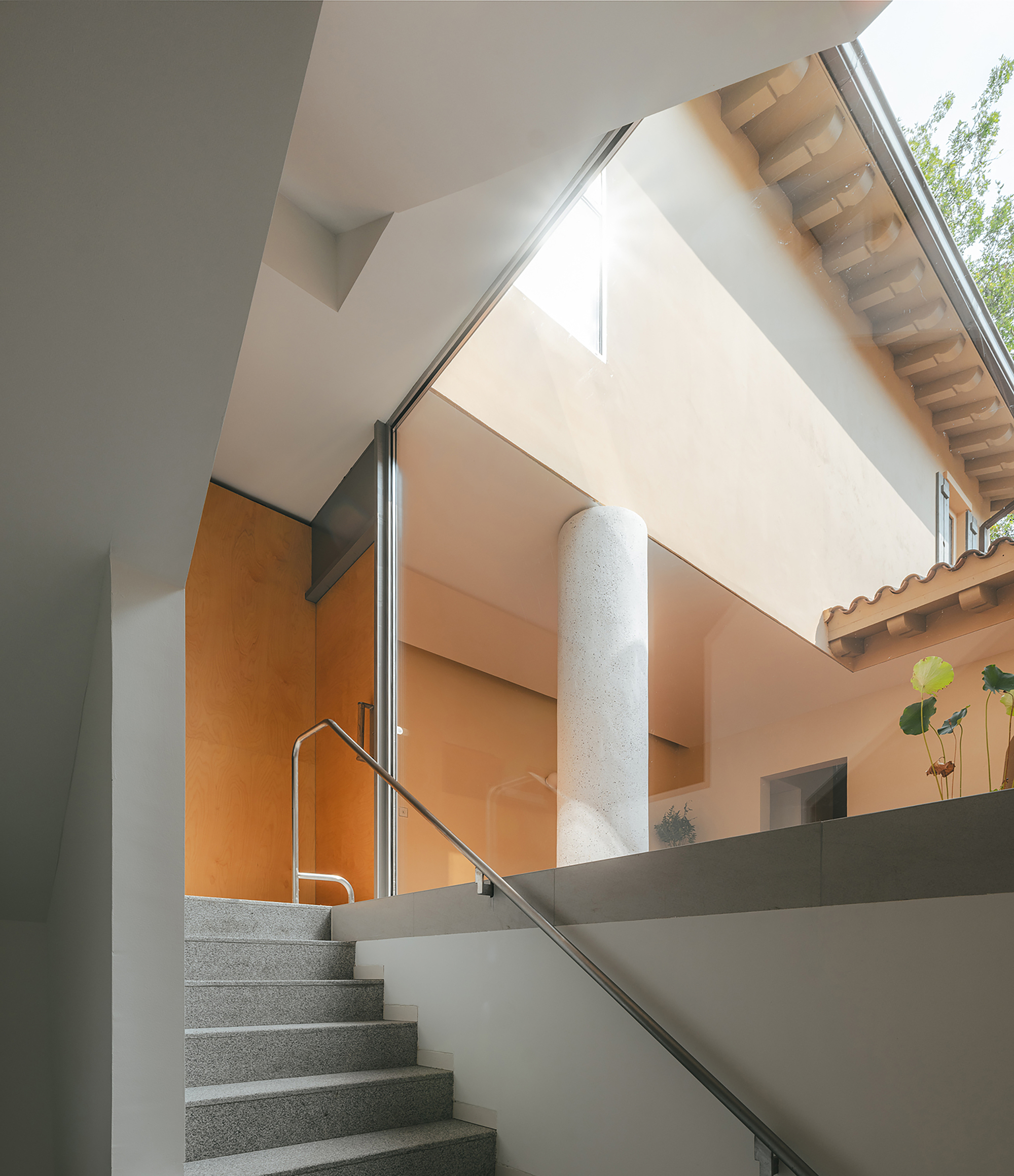 Terrazzo staircase with stainless steel handrail rising toward a light-filled upper level