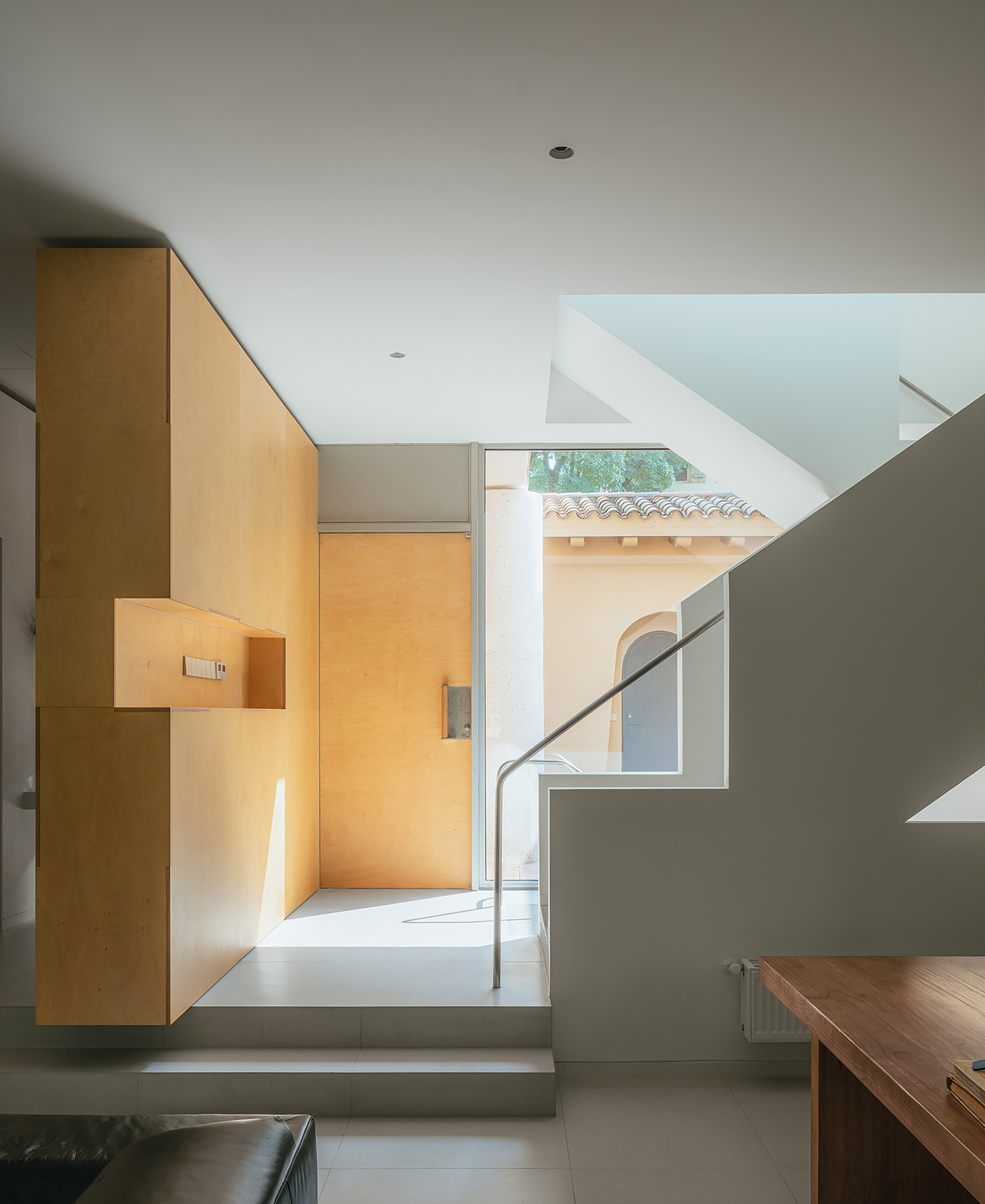 Entry hall with plywood storage wall and view through to courtyard with tile roof