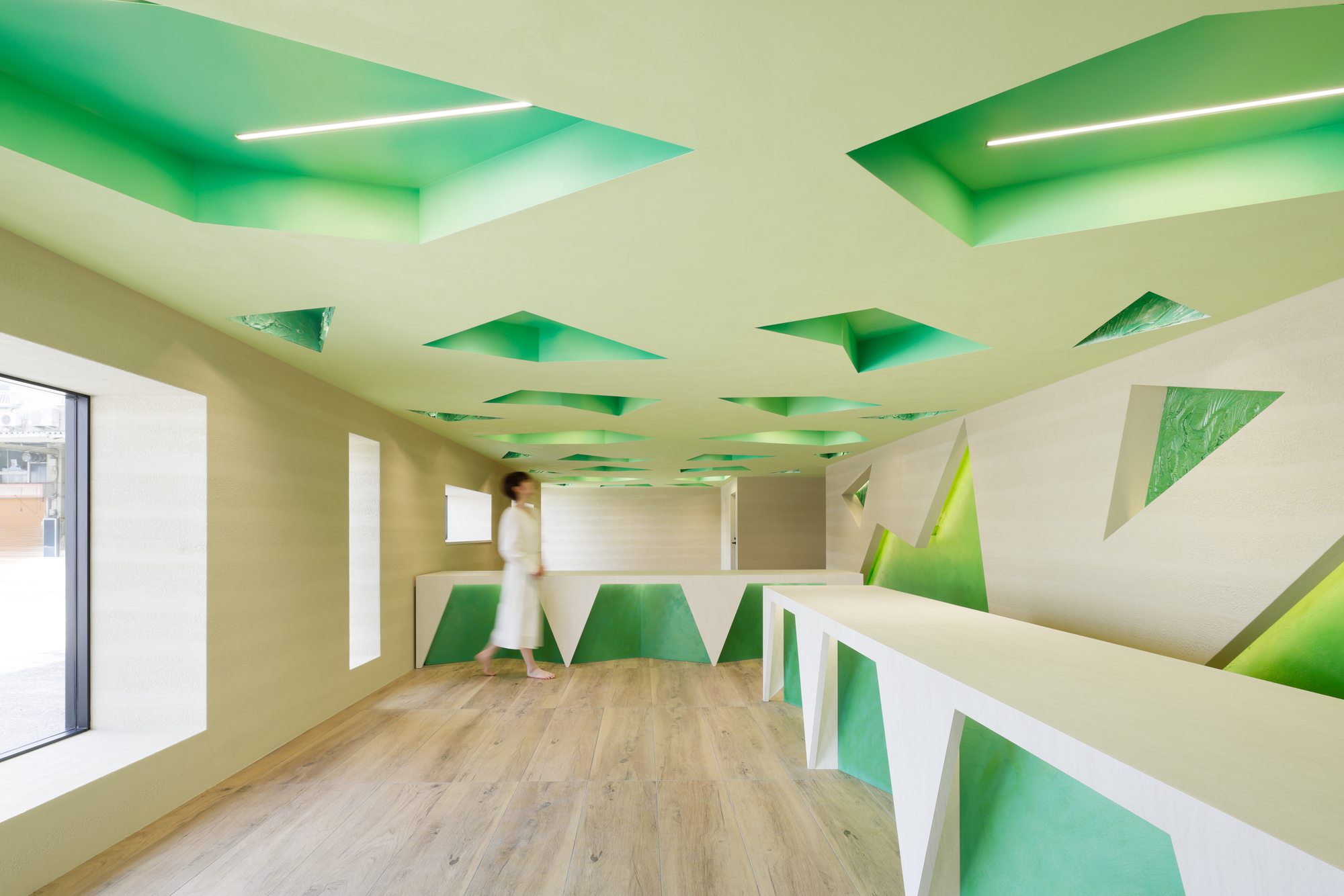 Wide view of the office interior with green-painted angular ceiling cavities and triangular wall recesses