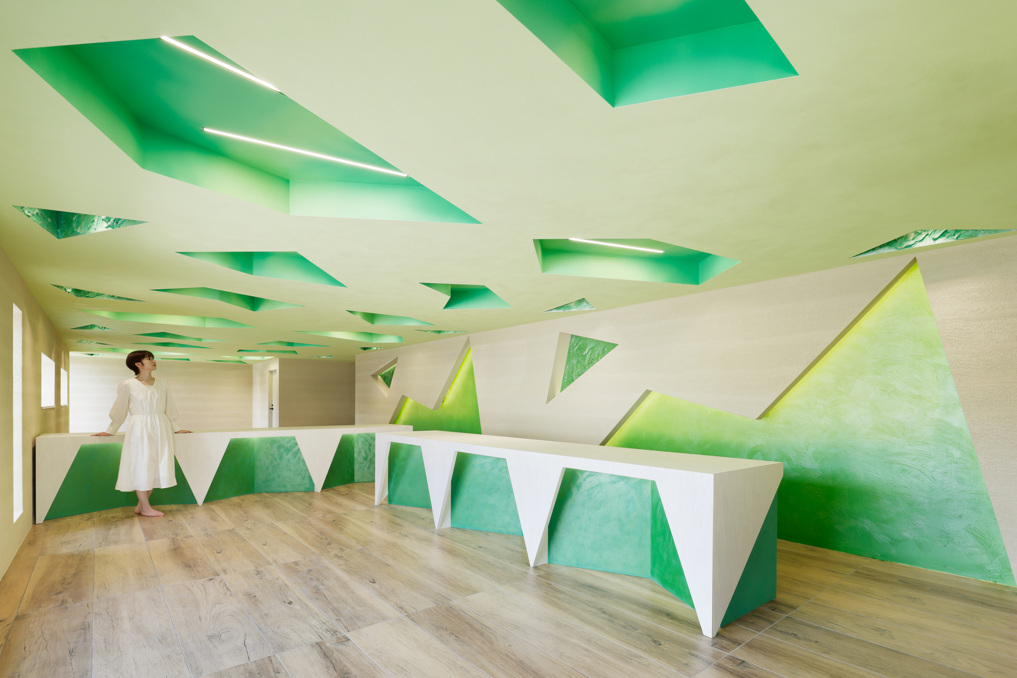 Faceted reception counter with green inset panels and a sculpted ceiling above