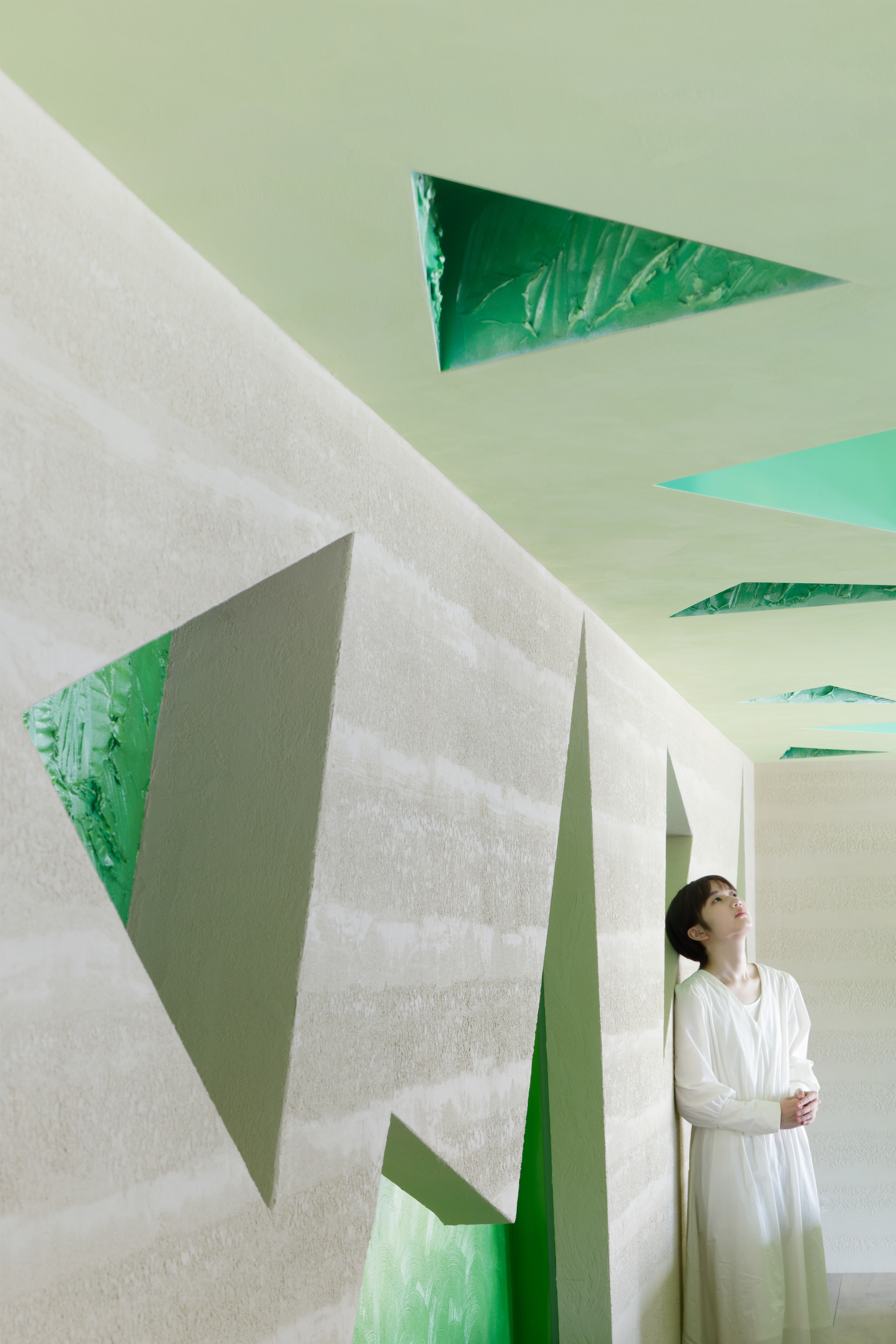 Tall corridor wall with embedded triangular green panels and a figure looking up