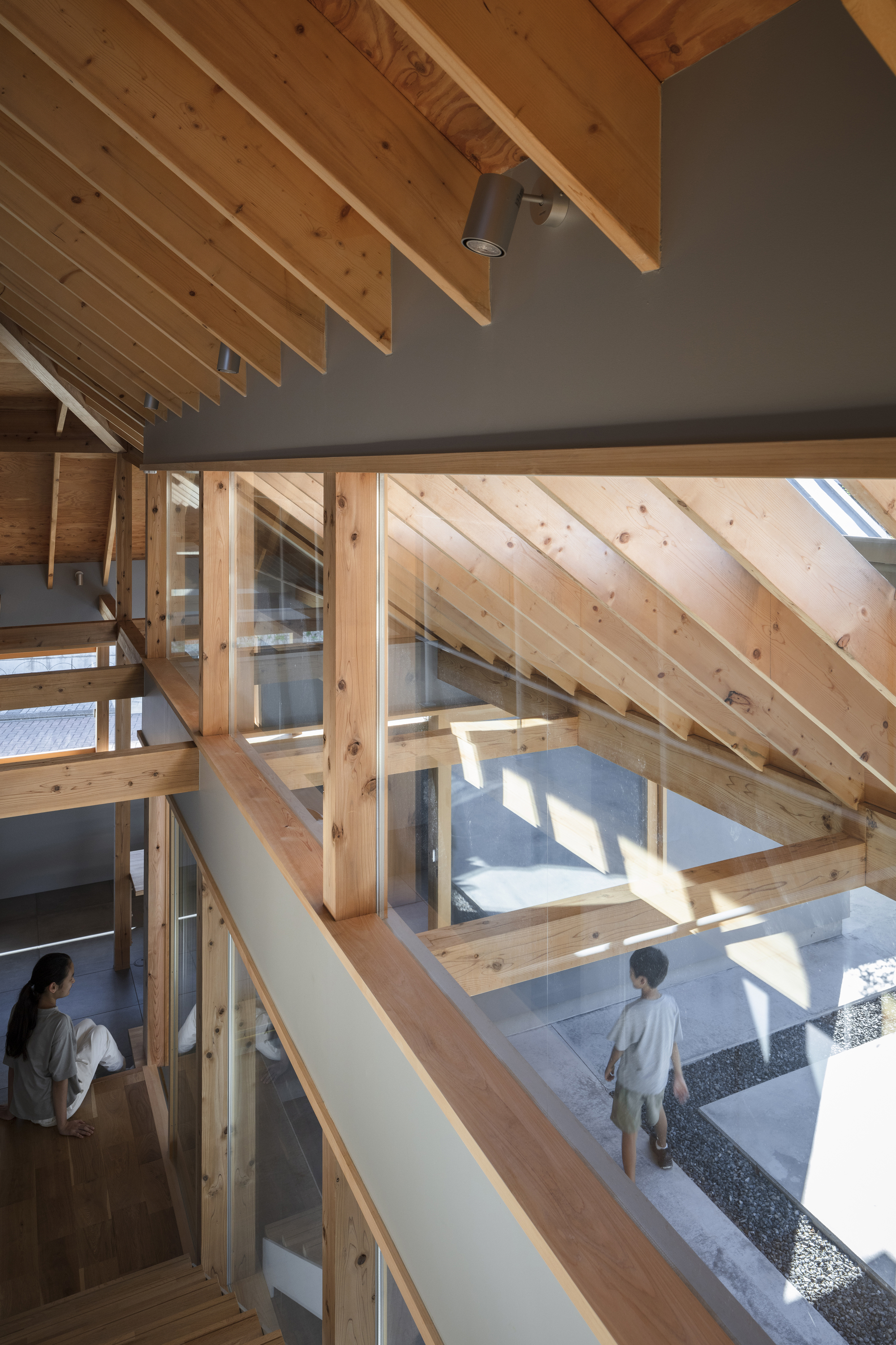 View through timber framing to courtyard below where a person stands in sunlight