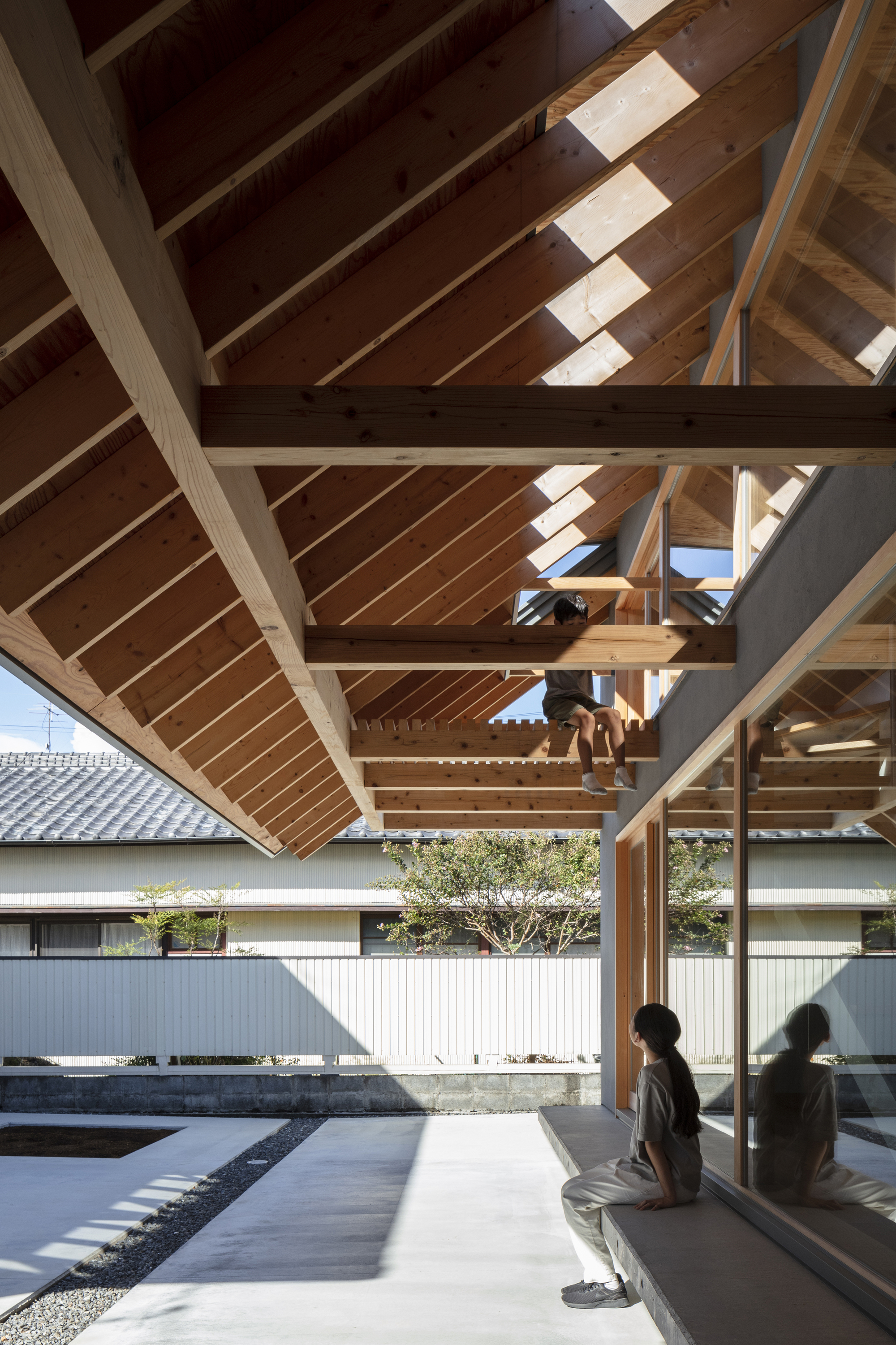 Covered terrace with exposed timber frame and rafters as two figures sit overlooking the courtyard