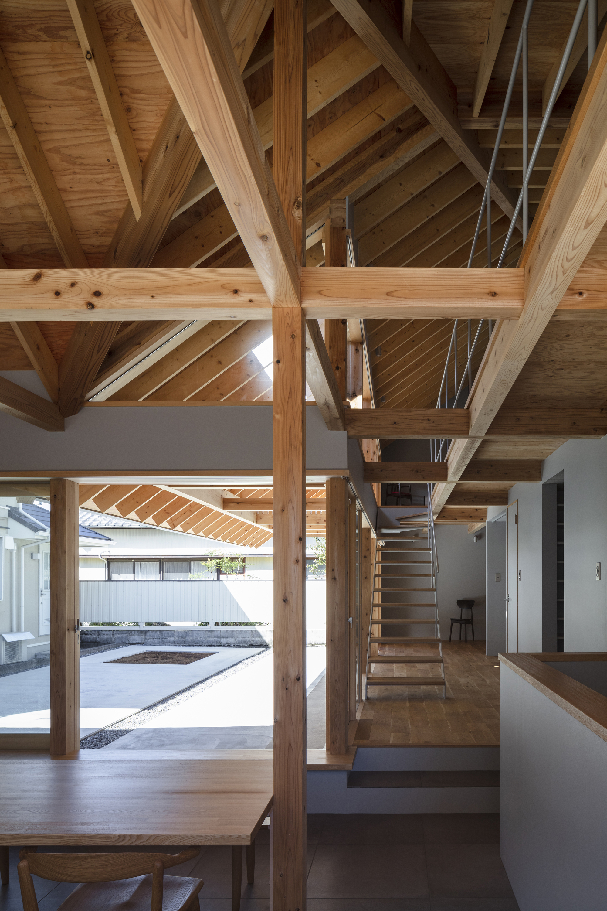 Interior living space showing timber post-and-beam structure with open staircase and view to courtyard