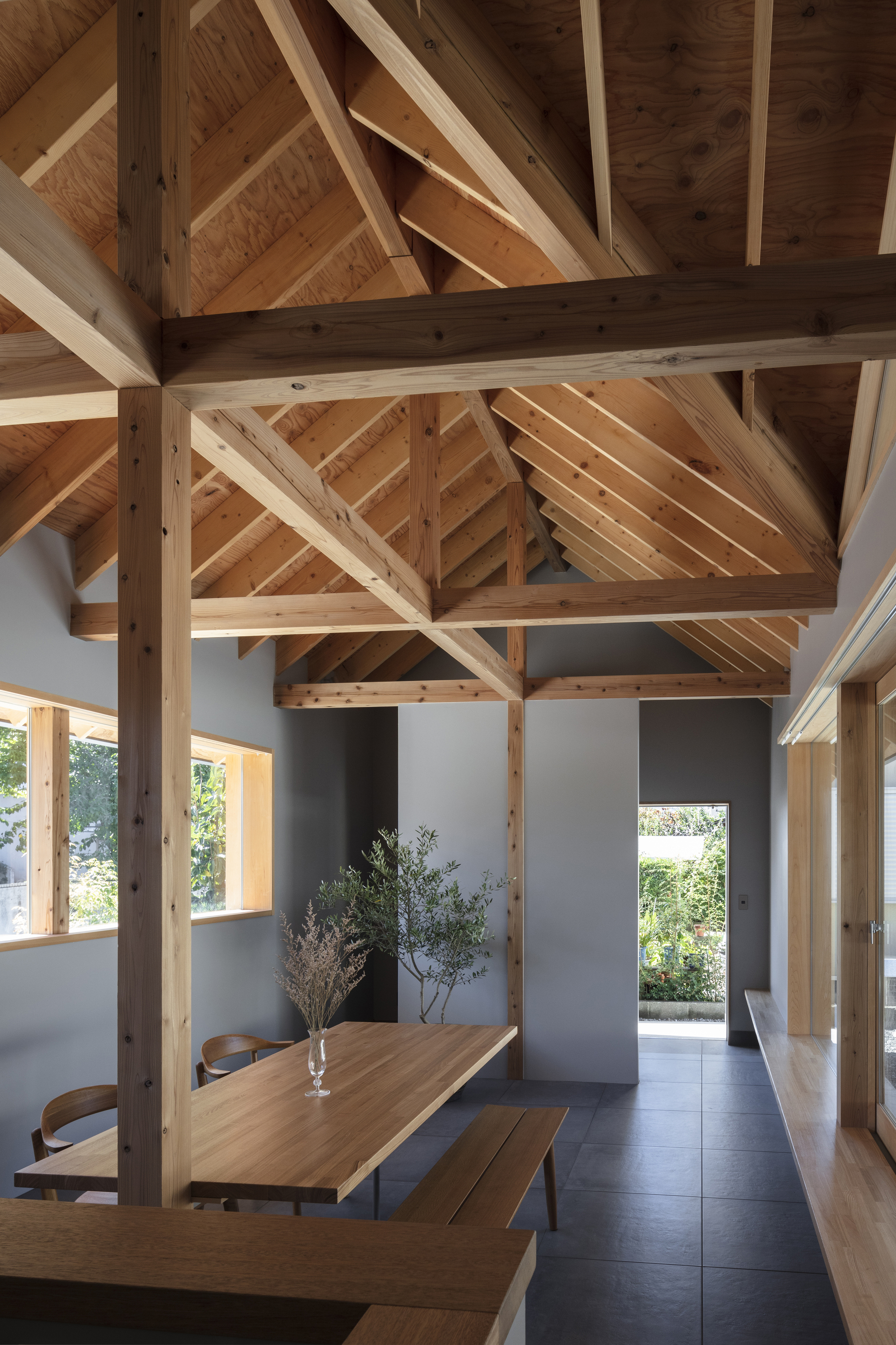 Dining area beneath exposed timber trusses with a vase of branches on the table