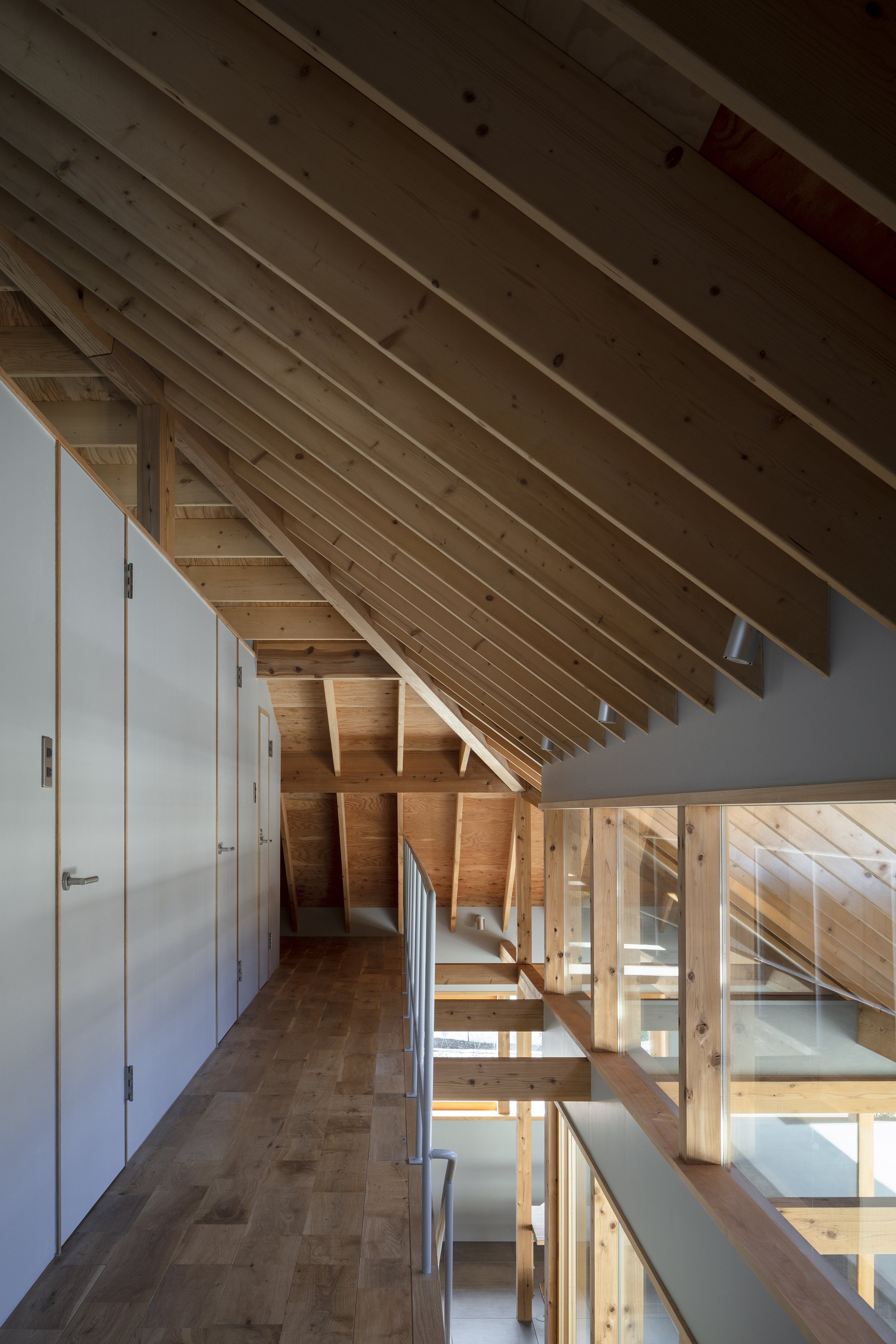 Upper level hallway with exposed timber roof beams and glass-paneled railing overlooking the floors below