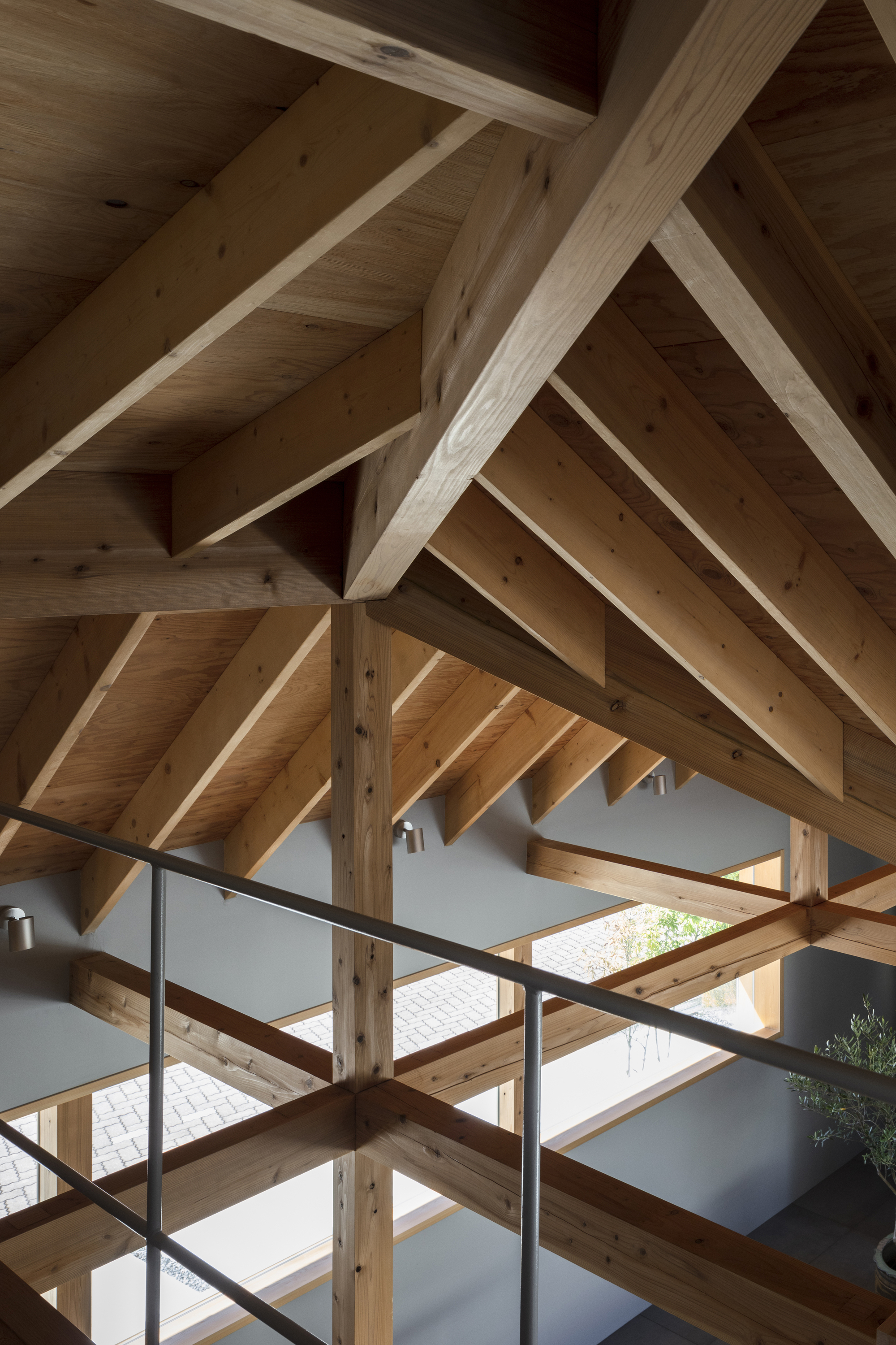 Upward view of the timber roof structure with interlocking beams and rafters above a steel railing