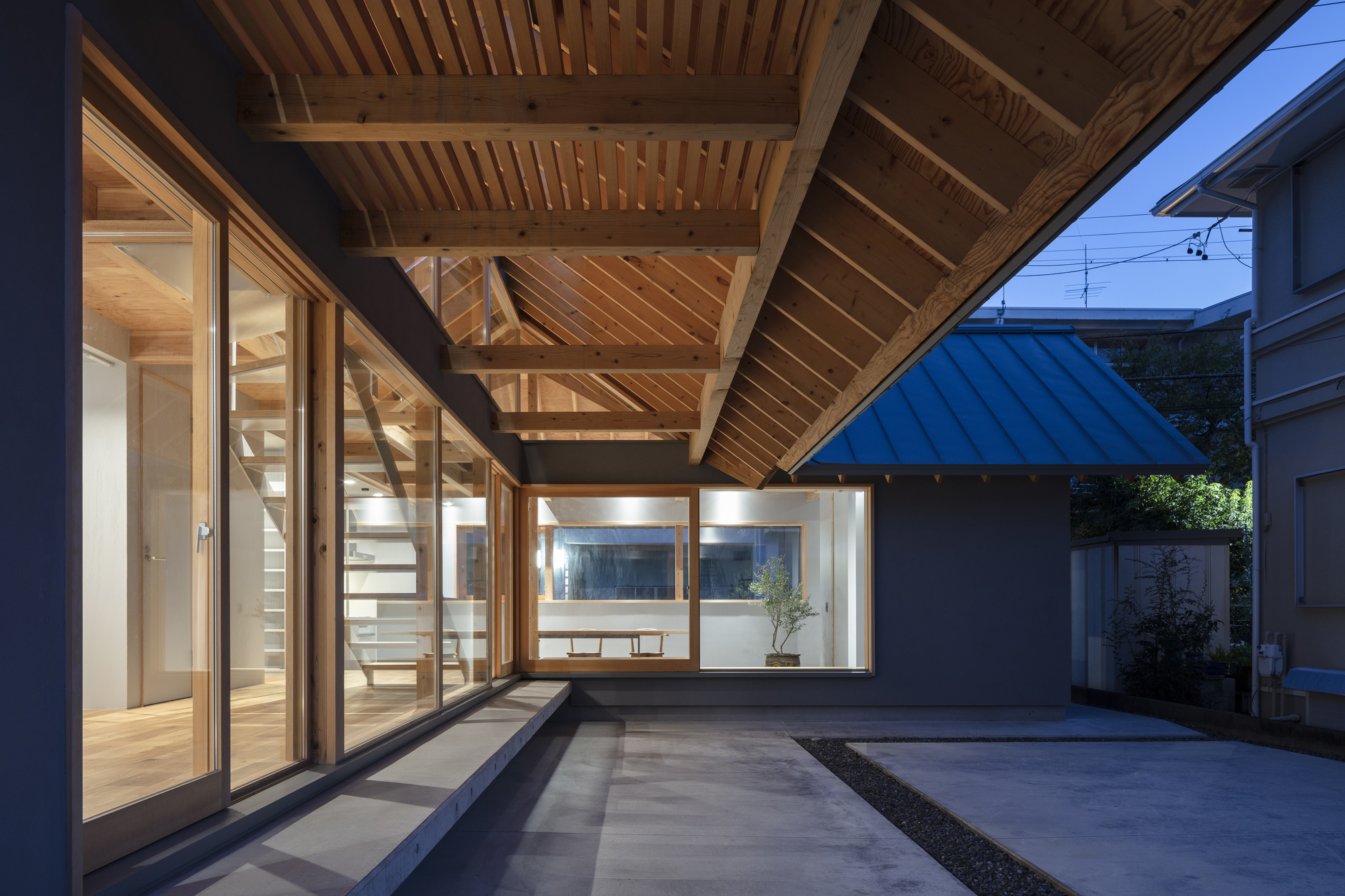Courtyard view showing timber-framed glazing beneath a cantilevered roof with slatted ceiling at twilight