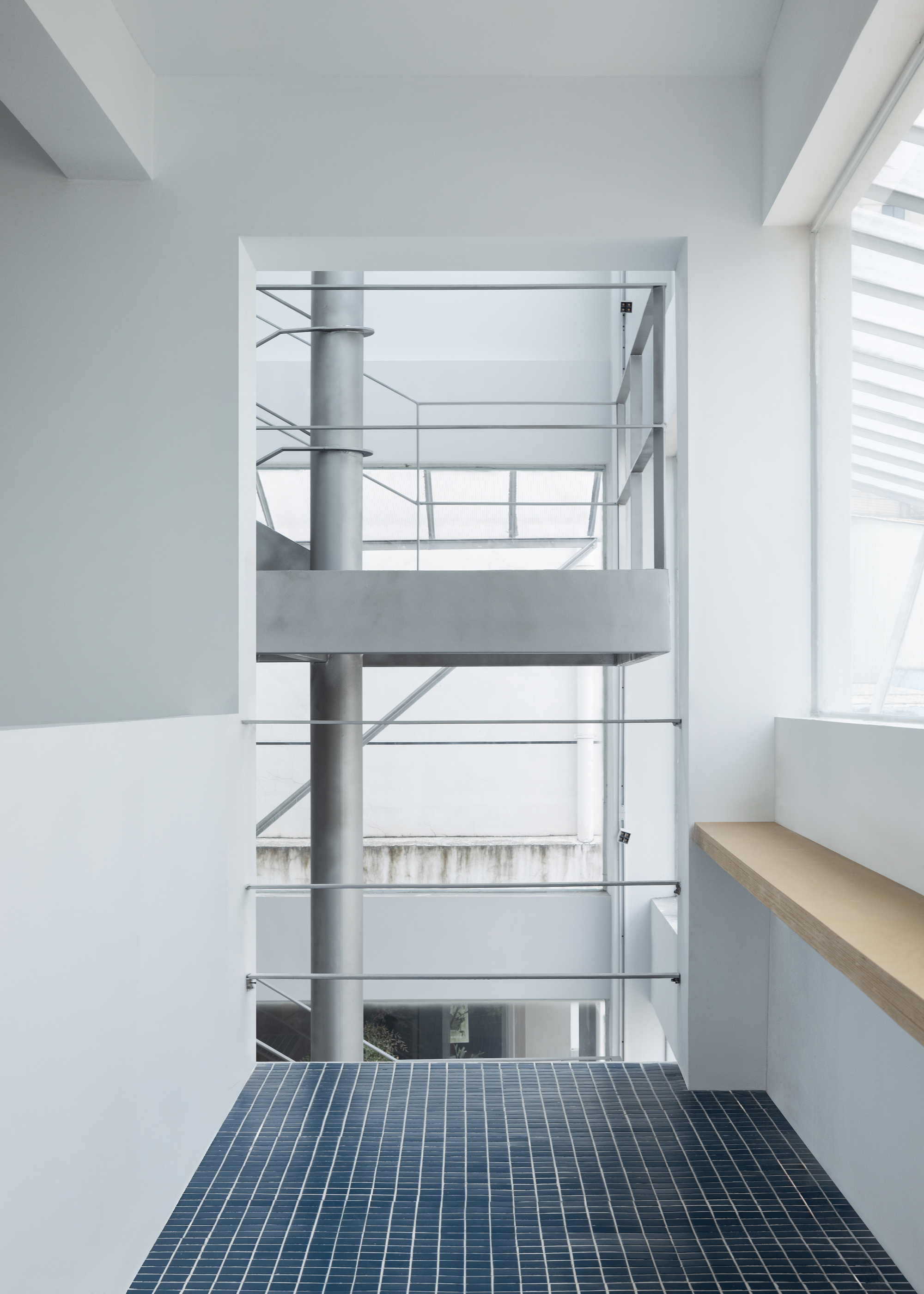 Interior balcony with blue mosaic tile floor overlooking a multi-level atrium with steel railings
