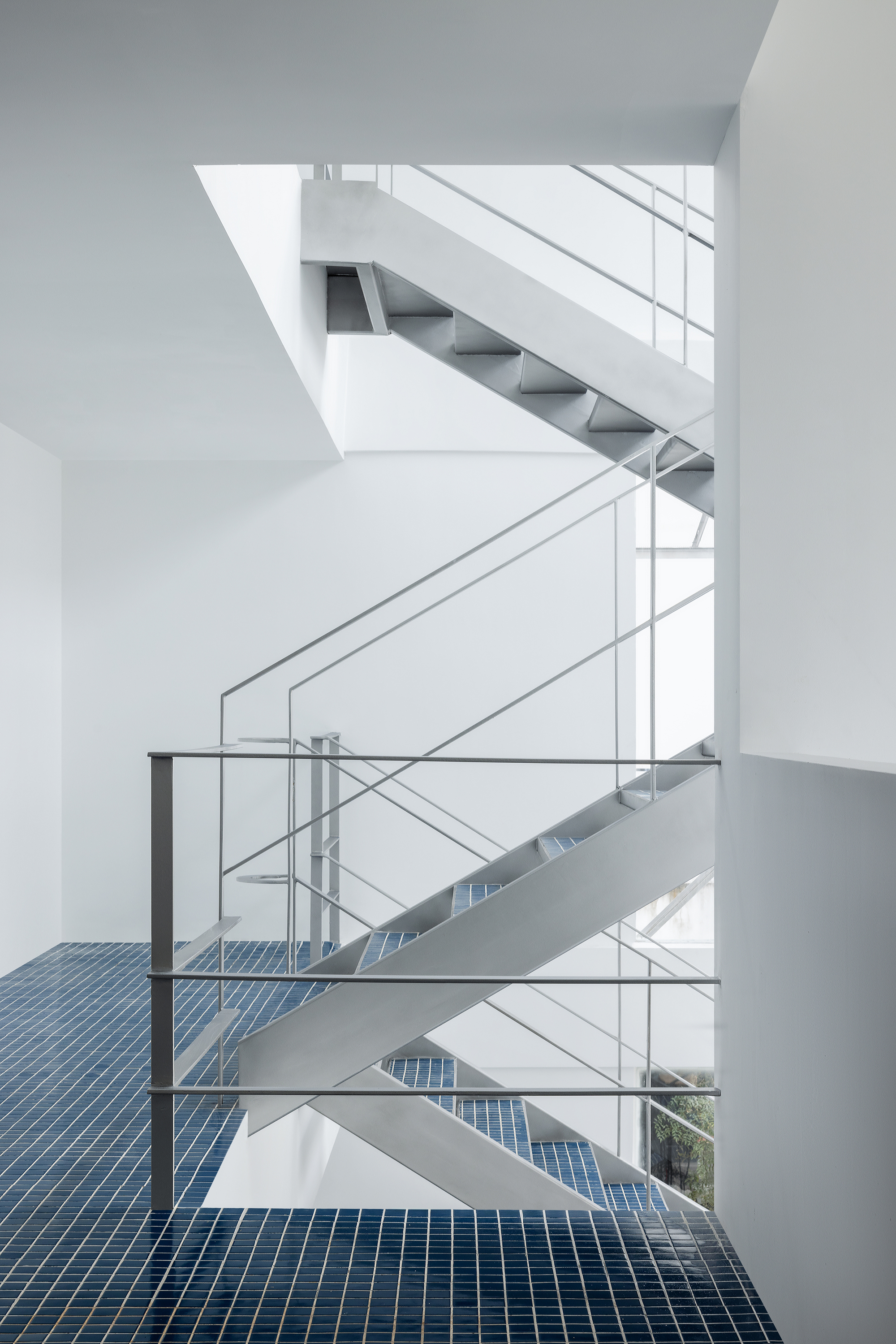 Vertical atrium view showing switchback steel staircases connecting floors with blue mosaic tile landings