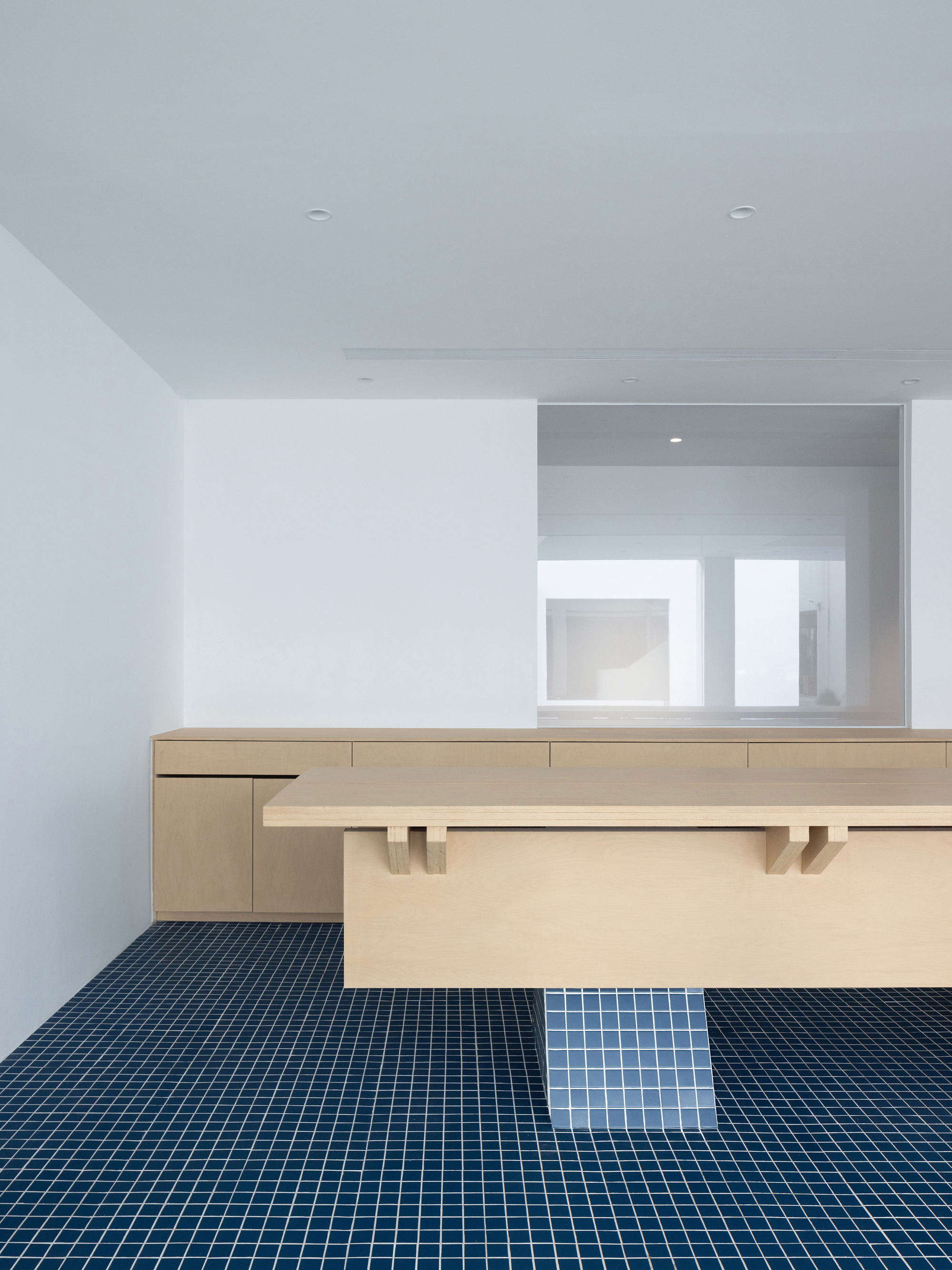 Light wood reception desk with blue mosaic tile floor and white walls under ceiling spotlights