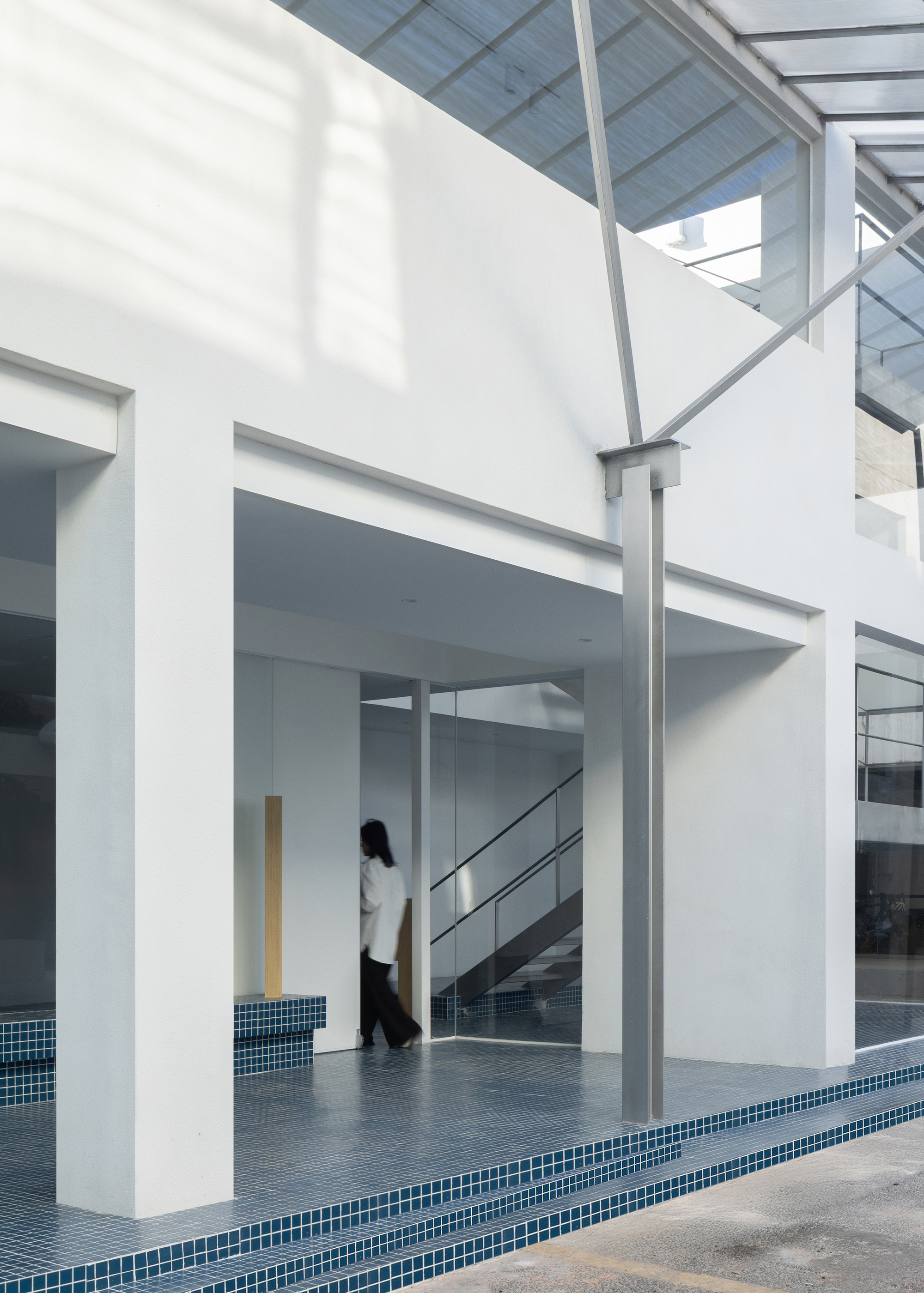 Courtyard threshold with blue mosaic tile edging and steel canopy framework overhead in daylight