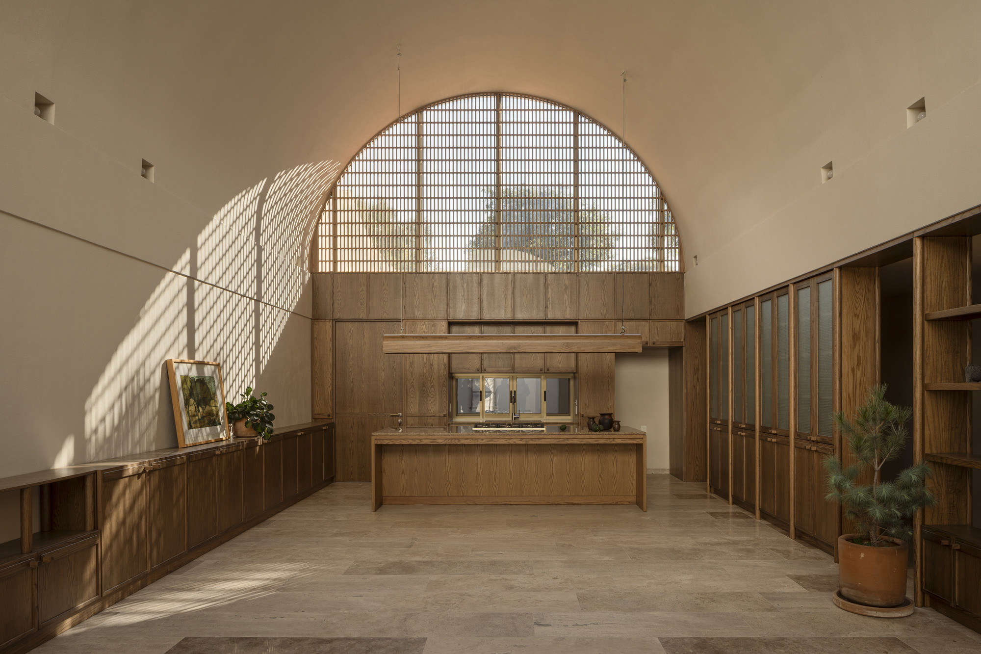 Interior space with arched gridded window casting diagonal shadows across wooden cabinetry and stone flooring