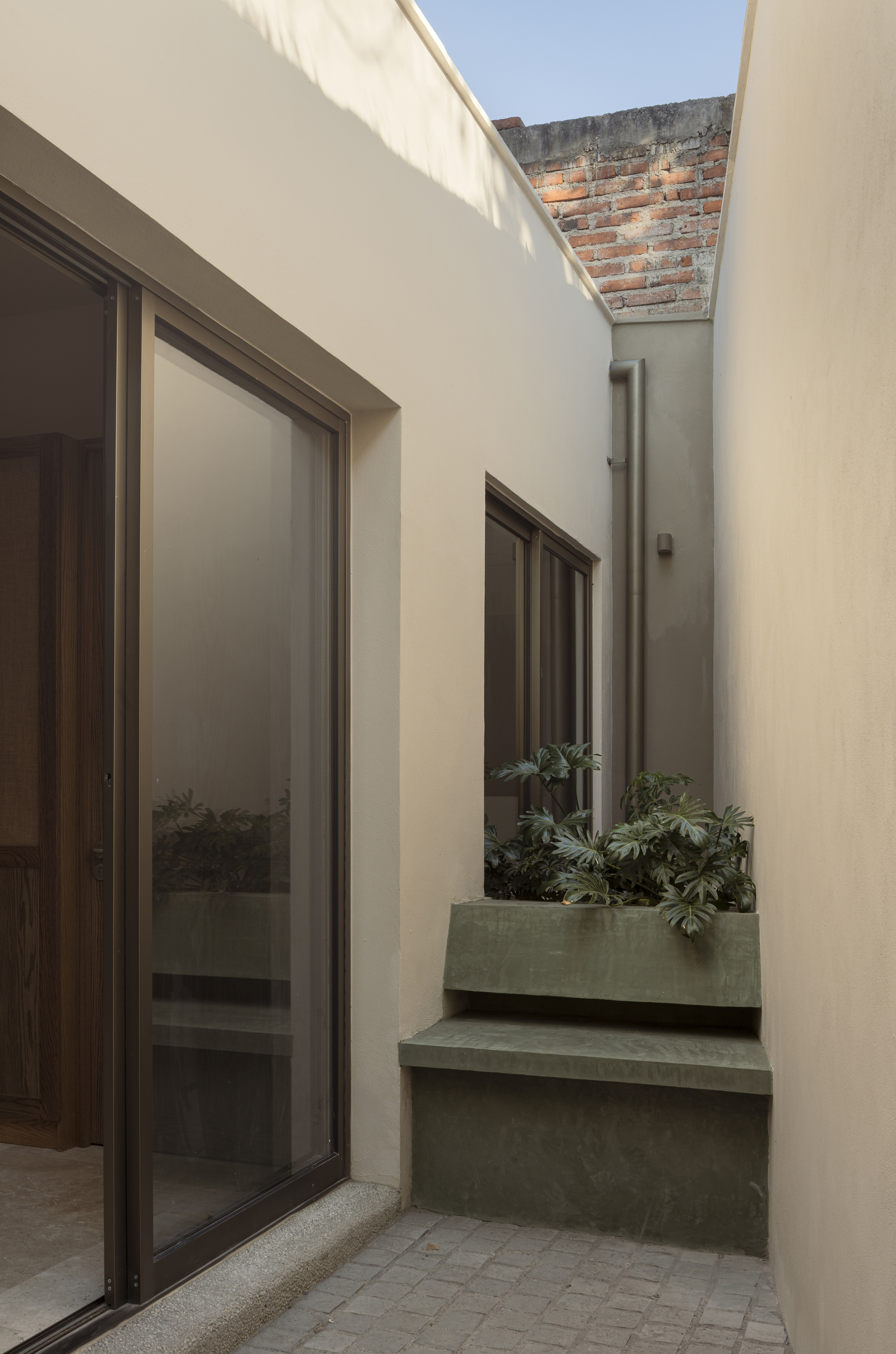 Narrow courtyard with tiered concrete planters and translucent roof panel casting soft light