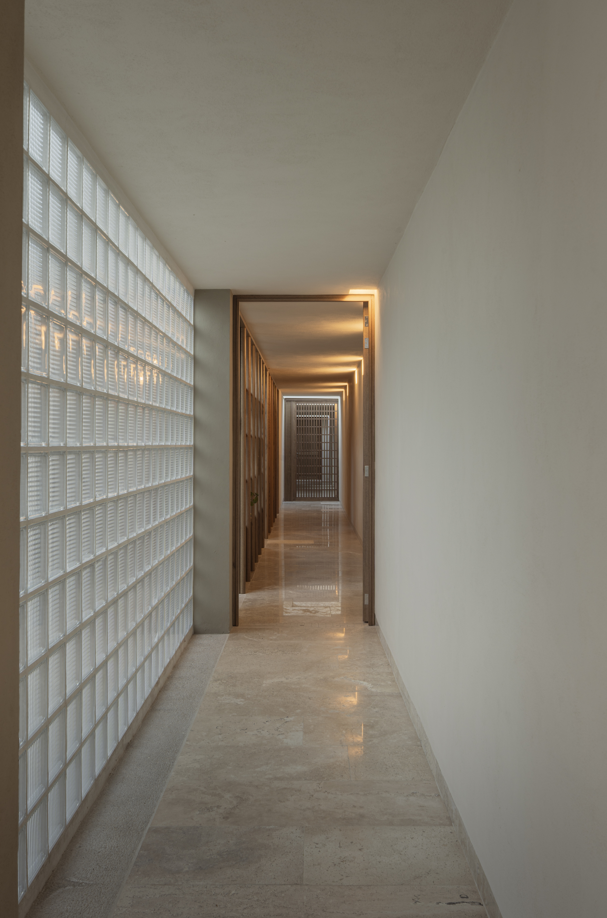 Long corridor with glass block wall filtering daylight along one side to timber doorways