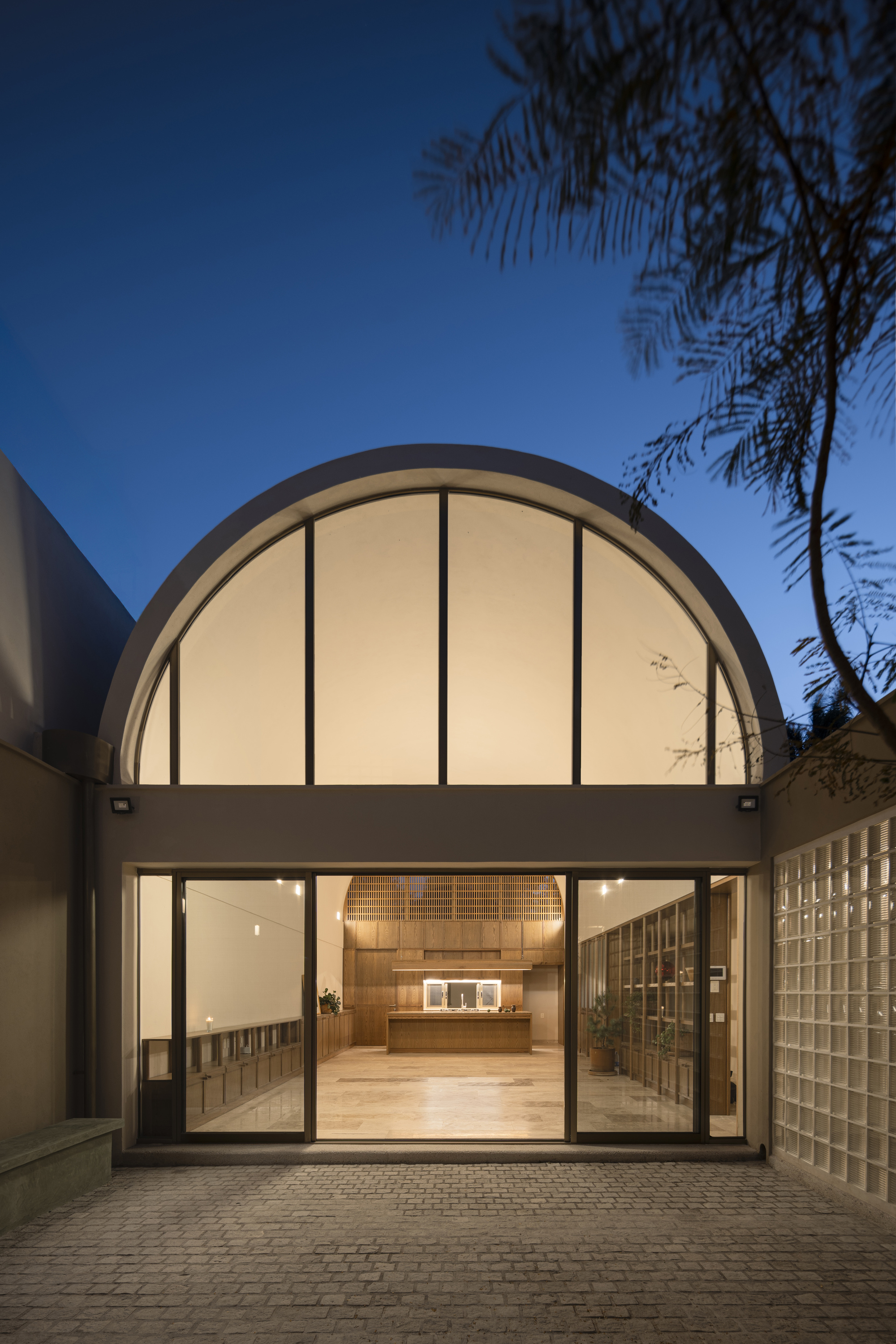 Illuminated arched facade at dusk with sliding glass doors and palm fronds overhead