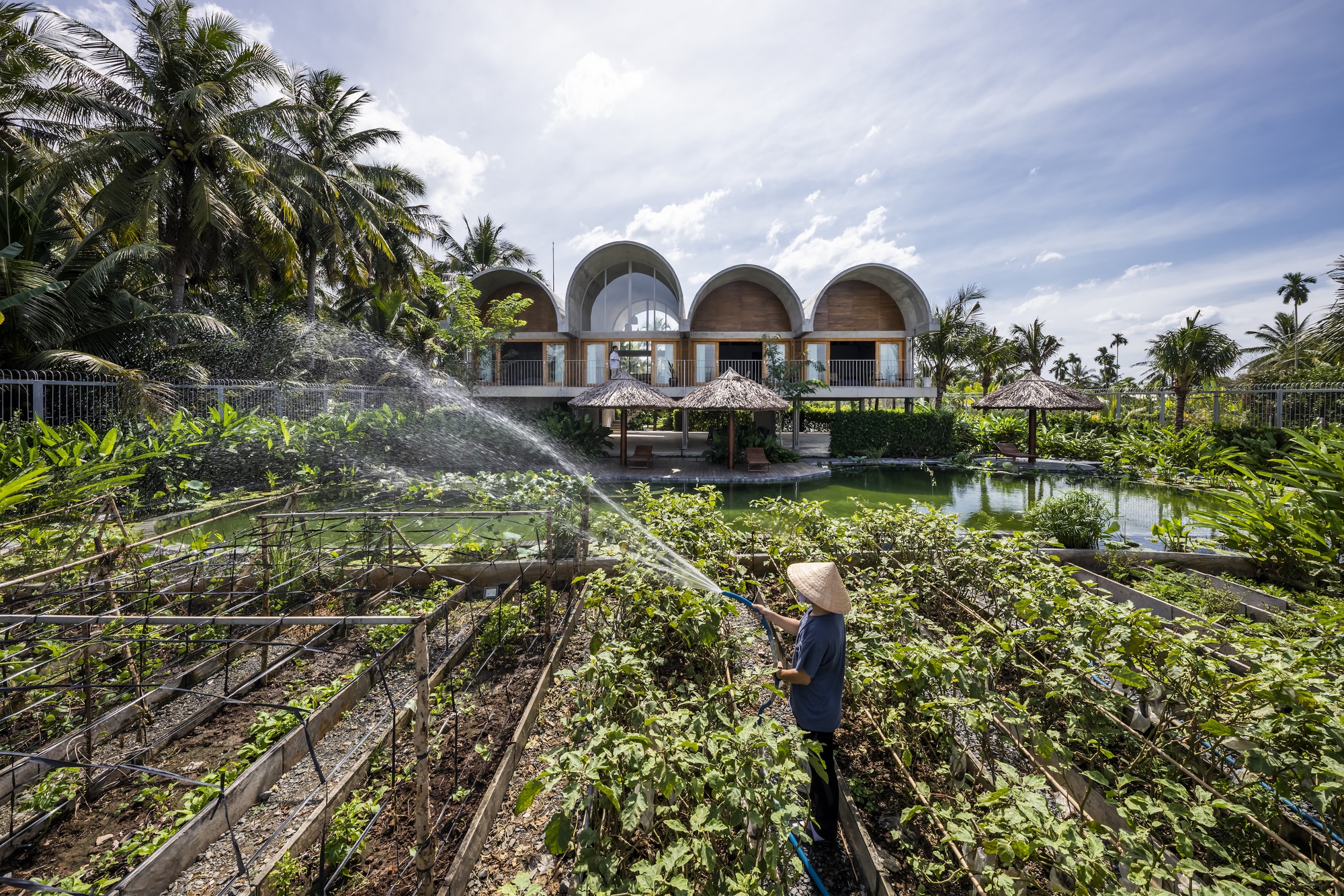 Worker tending vegetable beds with the arched roof structure and pond visible beyond