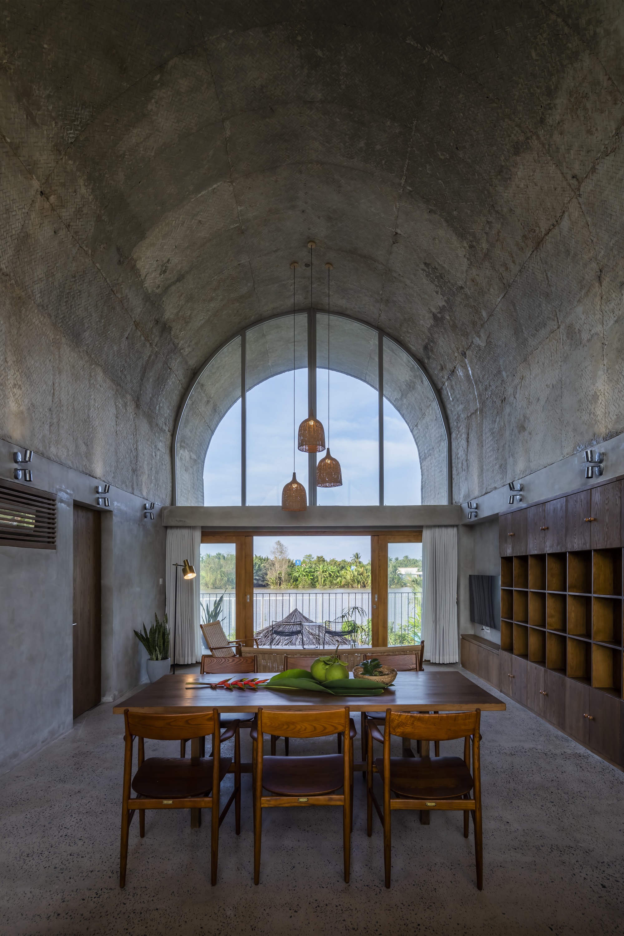 Dining area with vaulted concrete ceiling and arched window framing a view of the water beyond