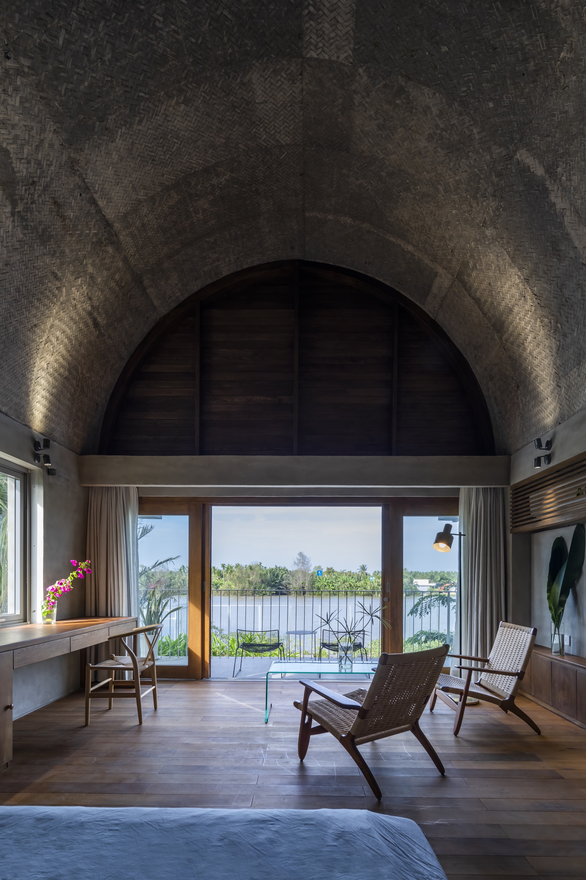 Interior view through arched opening with woven chairs beneath a vault illuminated by uplights