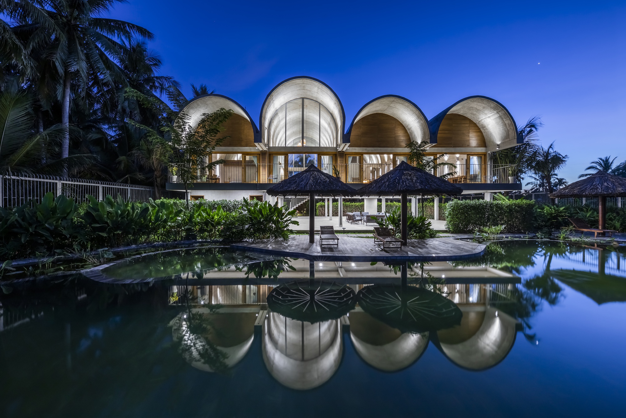Four barrel vaults reflected in the swimming pool at dusk with palm trees silhouetted behind
