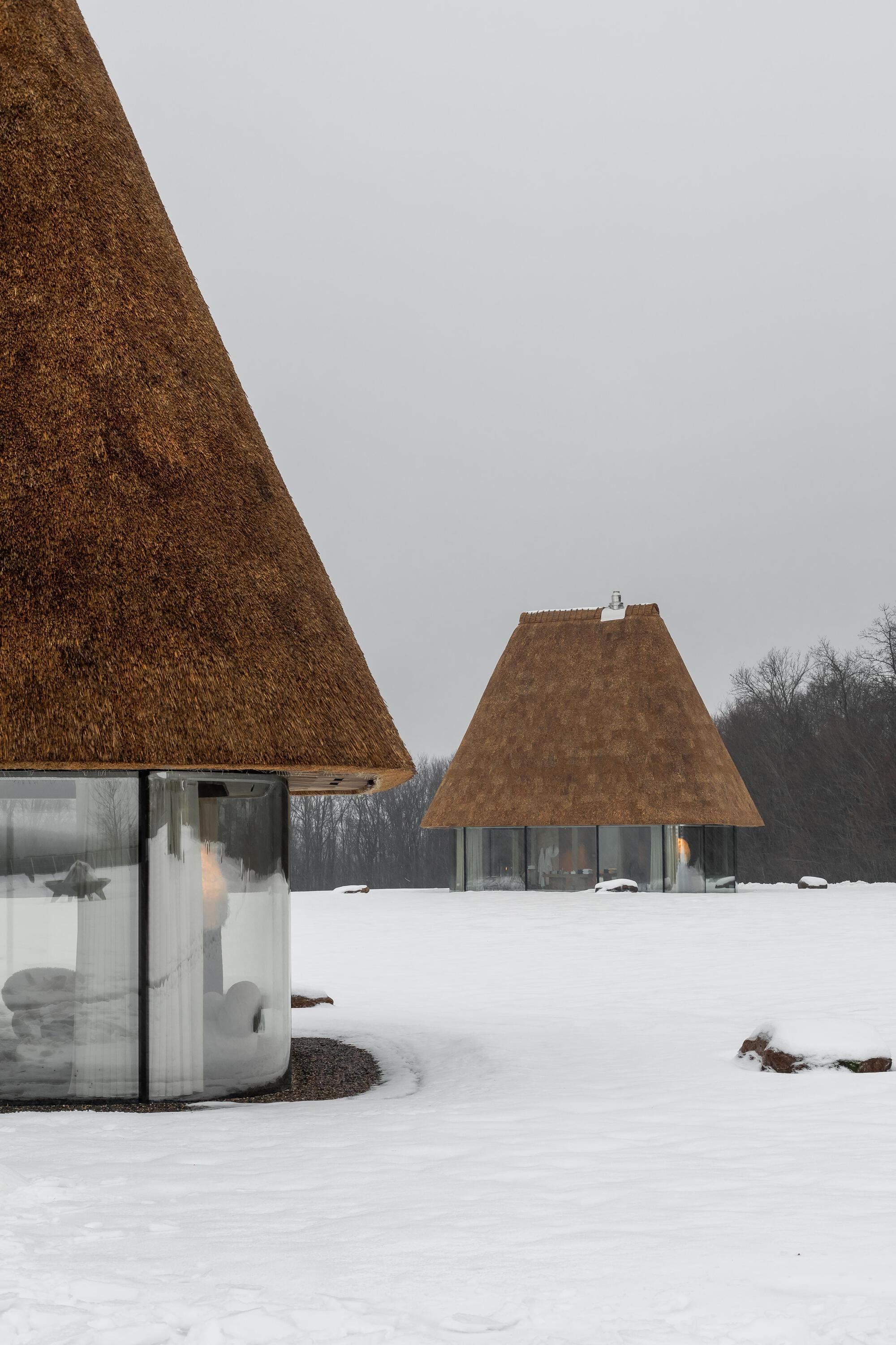 Two thatched roof pavilions on a snowy field with bare trees visible along the horizon