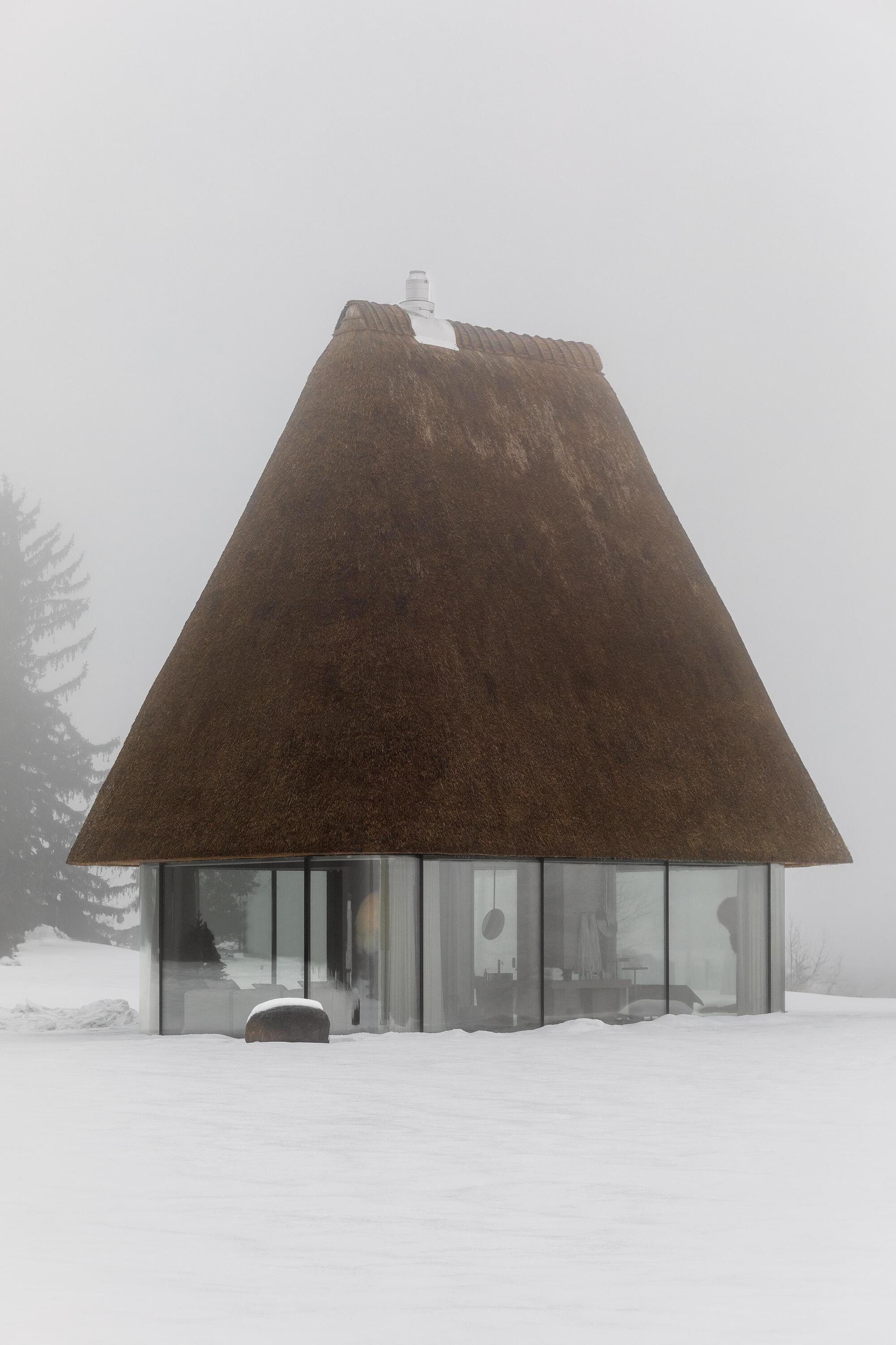 Thatched roof pavilion with glass walls surrounded by heavy snow and fog