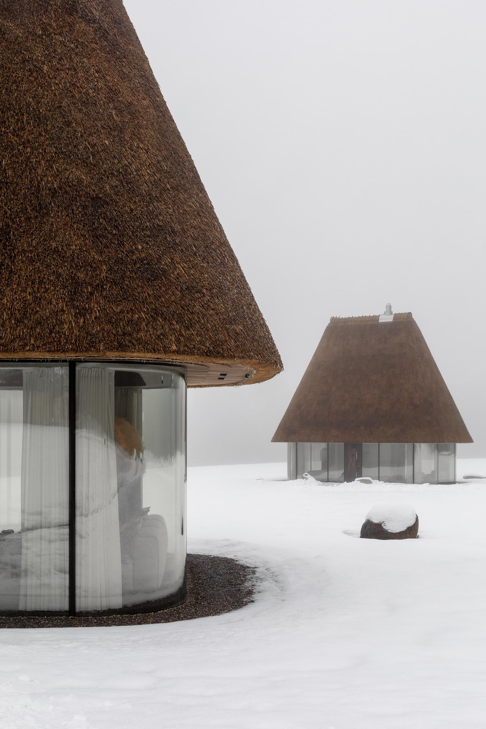 Two conical thatched volumes standing in a snow-covered field in misty conditions