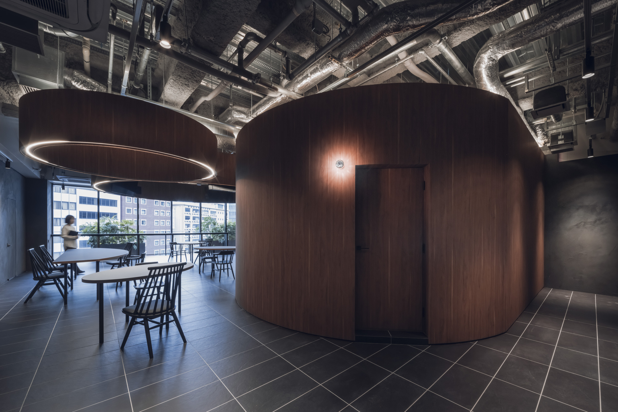 Curved walnut enclosure with dark tile flooring beneath exposed ductwork and concrete beams