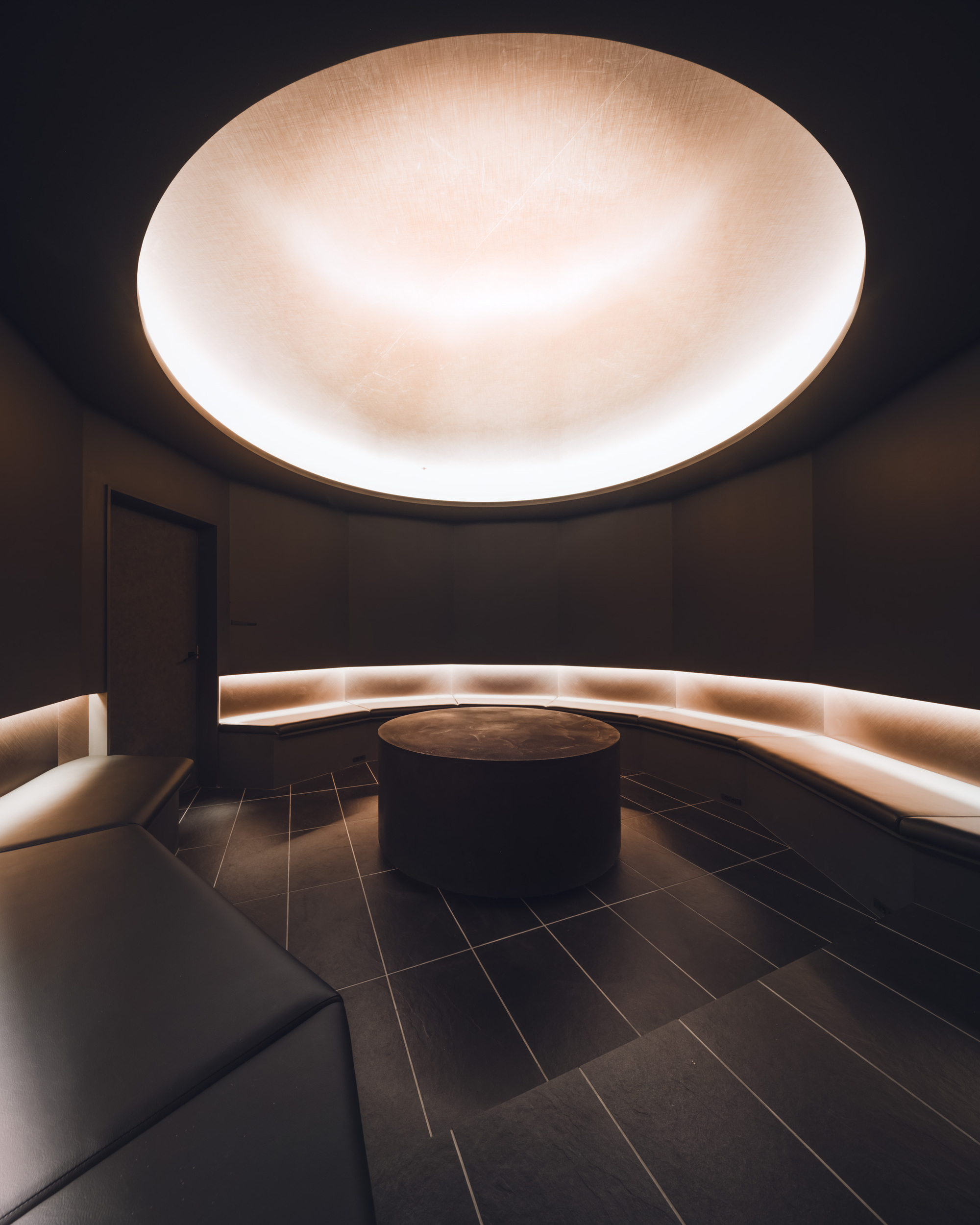 Circular seating alcove with backlit curved bench and illuminated dome ceiling in dark finishes